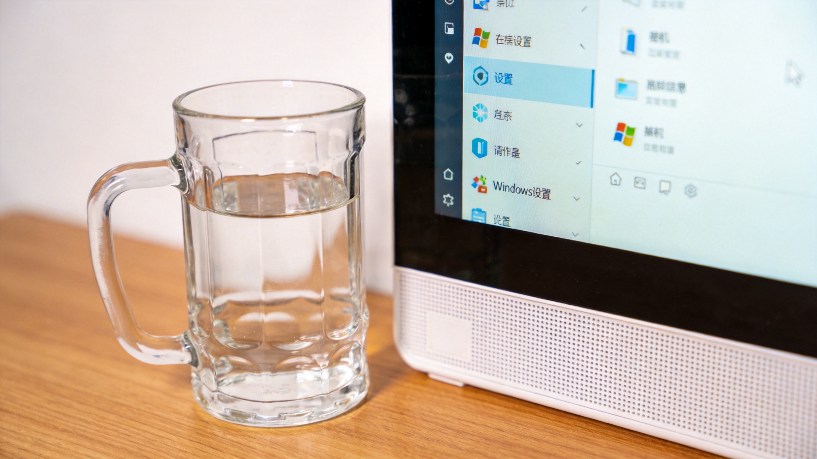 书桌上的主机，屏幕显示Windows设置界面，桌角放着水杯，自然光