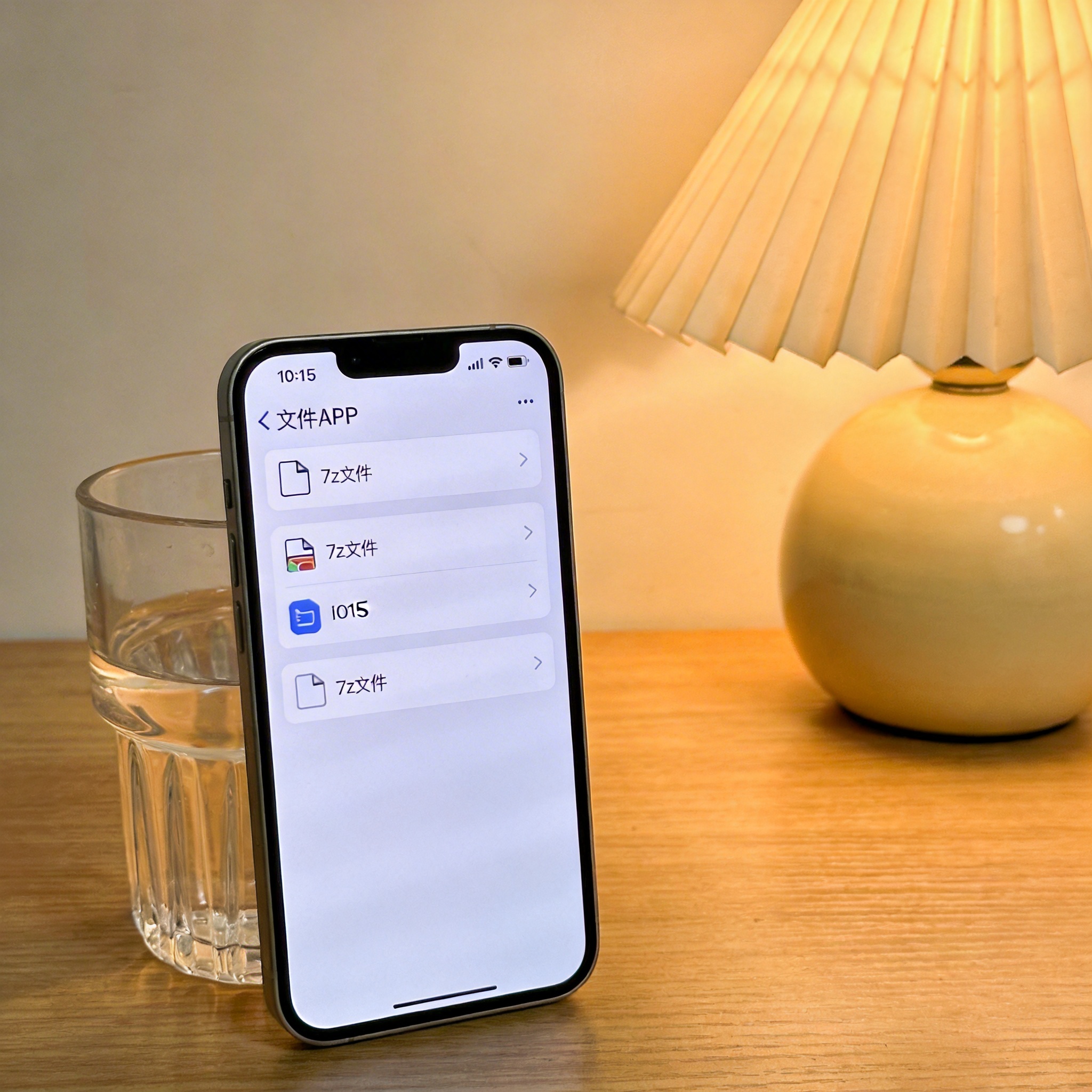 书桌上的苹果手机，屏幕显示文件APP里的7z文件图标，系统为iOS15，旁边放着半透明水杯，台灯暖光