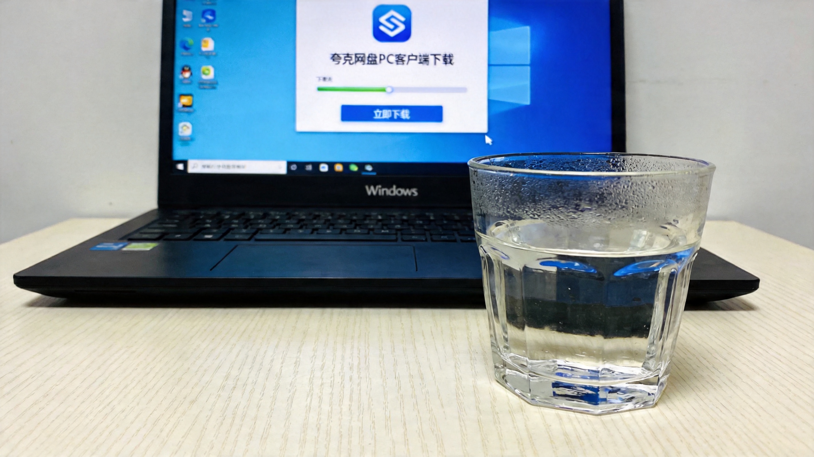 电脑桌的Windows系统电脑，屏幕显示夸克网盘PC客户端下载界面，旁边放着半杯凉白开，室内自然光