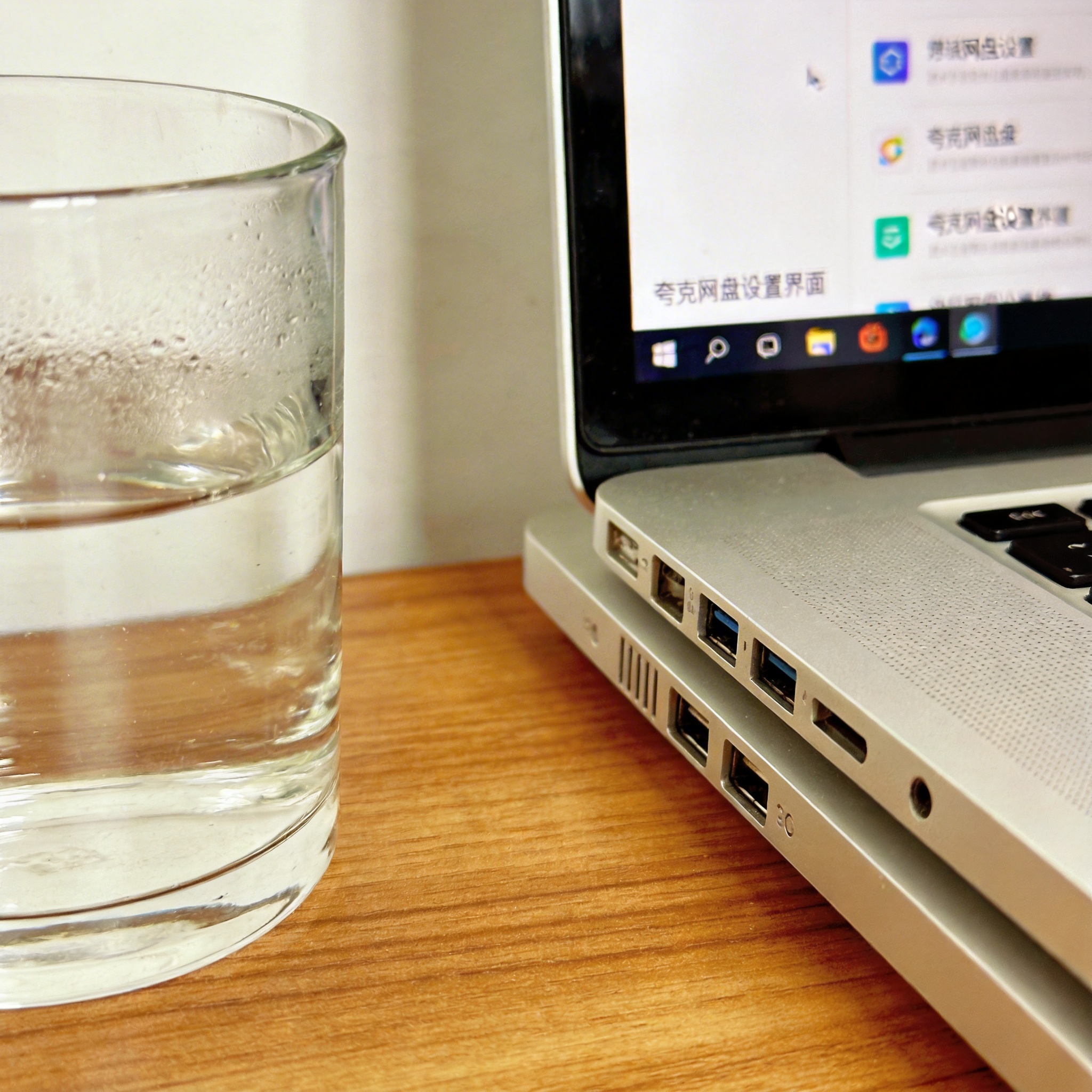 书桌上的主机，屏幕显示夸克网盘设置界面，桌角放着水杯，自然光
