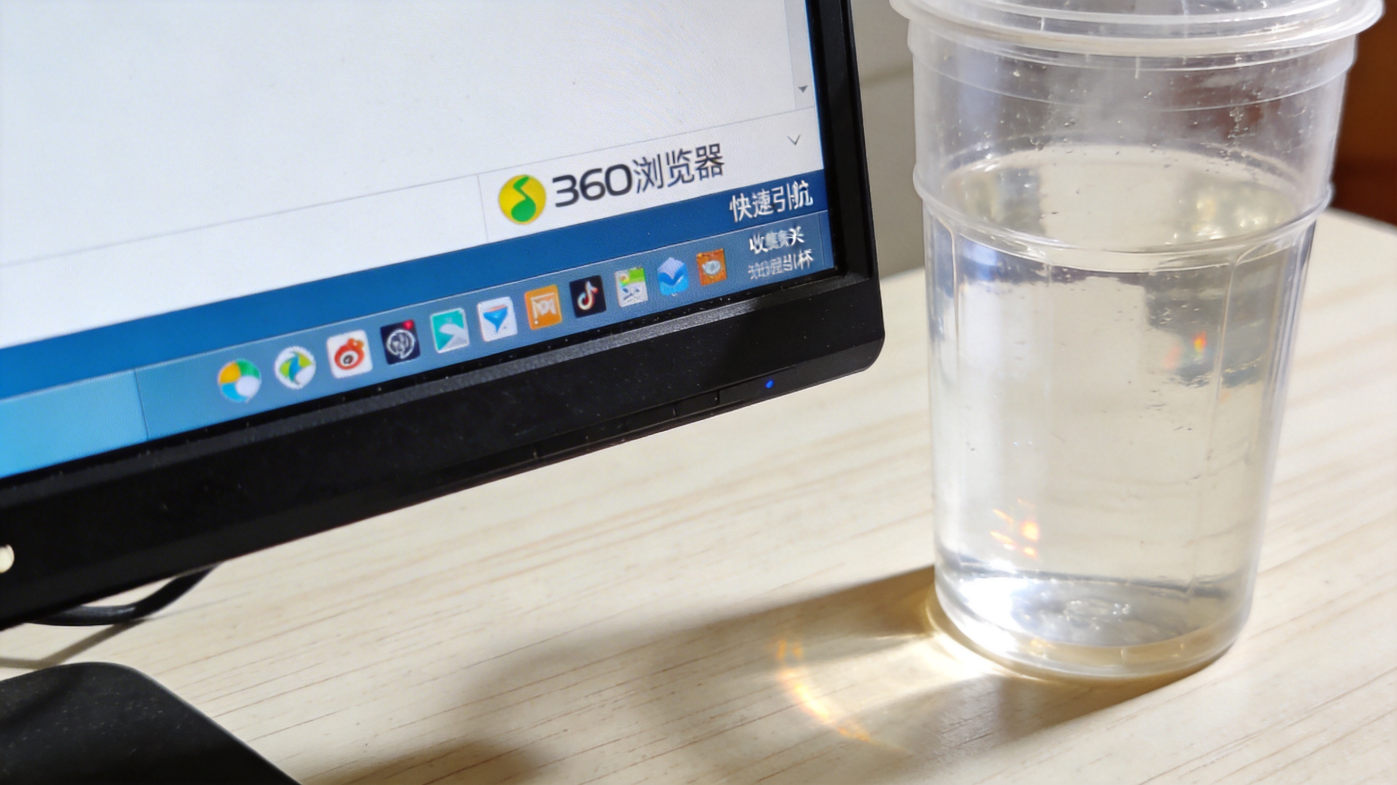 电脑桌面，屏幕显示360浏览器的收藏夹快速启动栏，栏里有常用网站图标，旁边放着塑料水杯，室内自然光