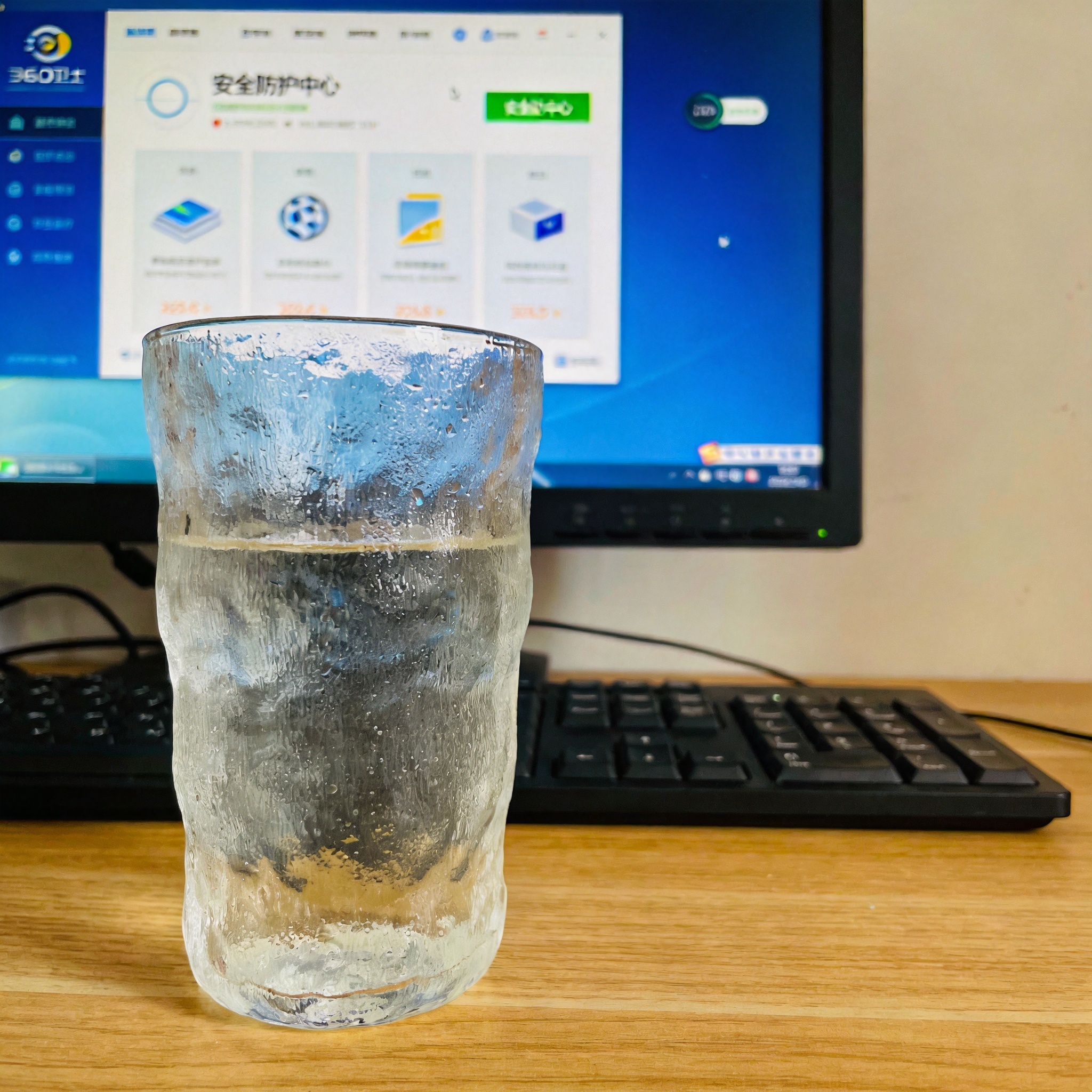 电脑桌的电脑屏幕显示360卫士主界面，首页有“安全防护中心”入口，旁边放着半杯凉白开，室内自然光