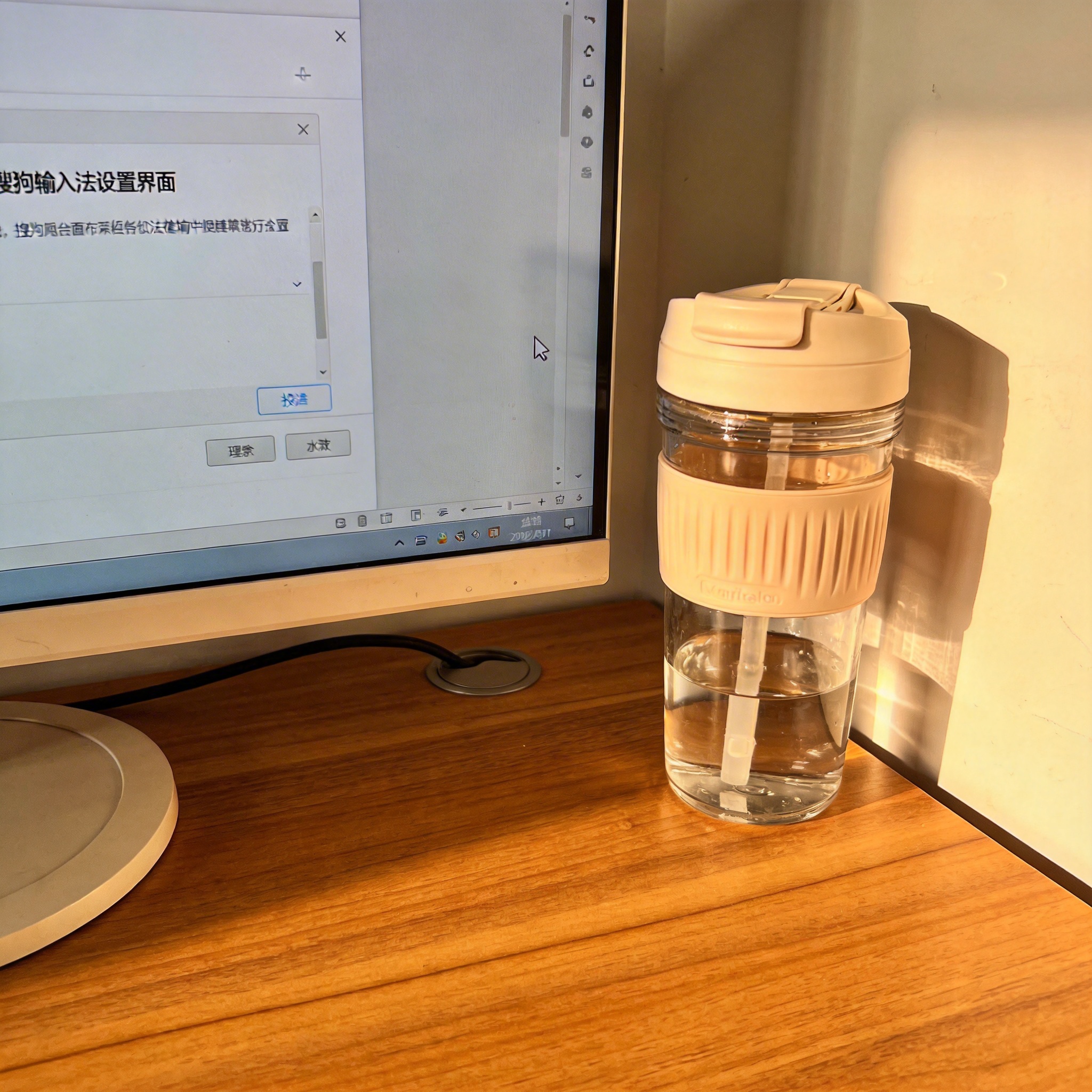 书桌上的主机，屏幕显示搜狗输入法设置界面，桌角放着水杯，自然光