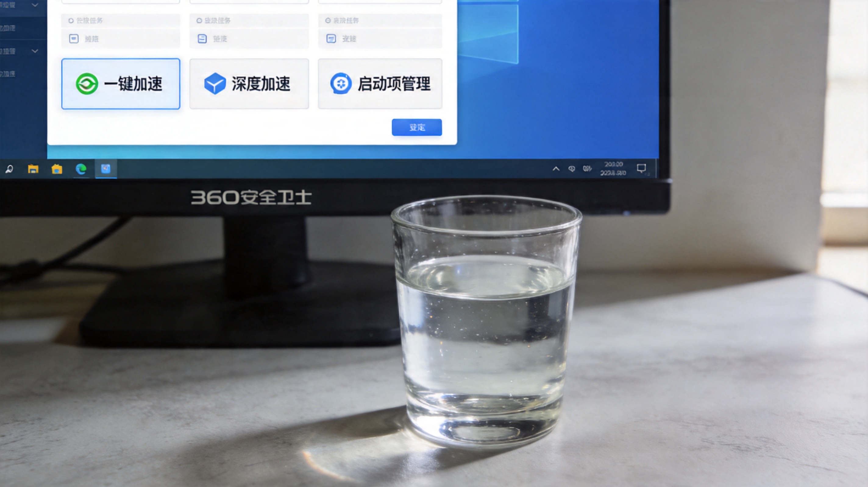 电脑桌面，屏幕显示360安全卫士系统加速界面，界面上有“一键加速”“深度加速”“启动项管理”板块，桌面放着半杯水，室内自然光