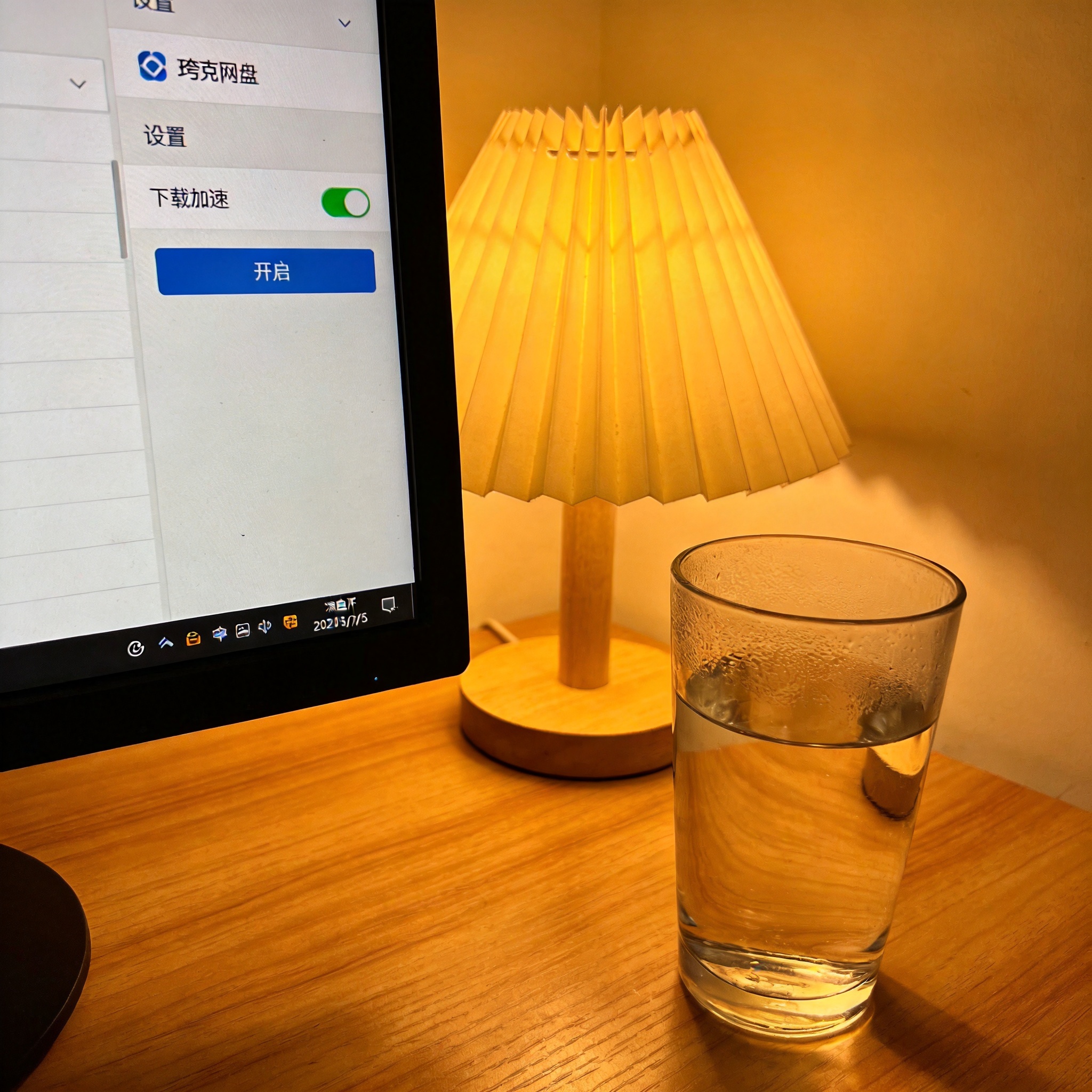 电脑屏幕显示夸克网盘设置界面，“下载加速”选项处于开启状态，桌面角落放着半杯凉白开，台灯暖光