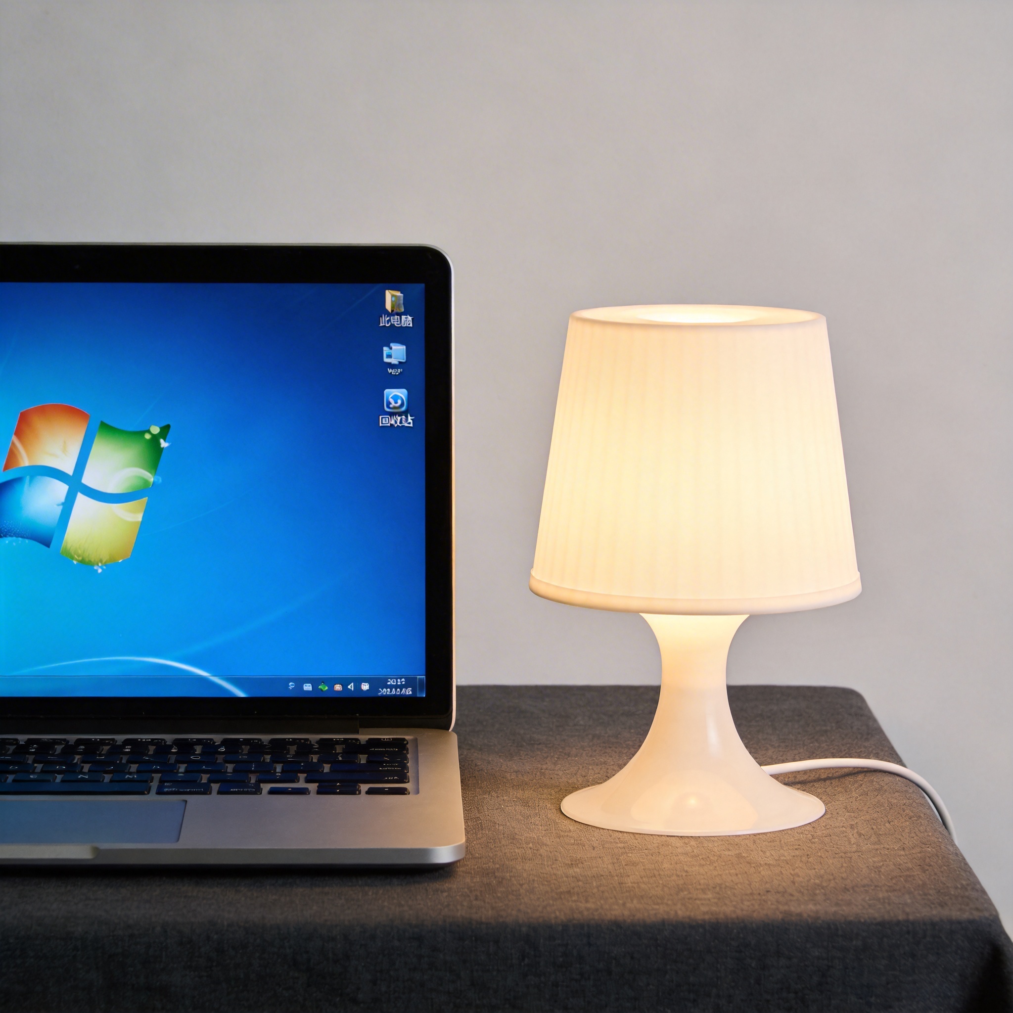 电脑桌上的电脑，屏幕显示Windows界面，旁边放着台灯