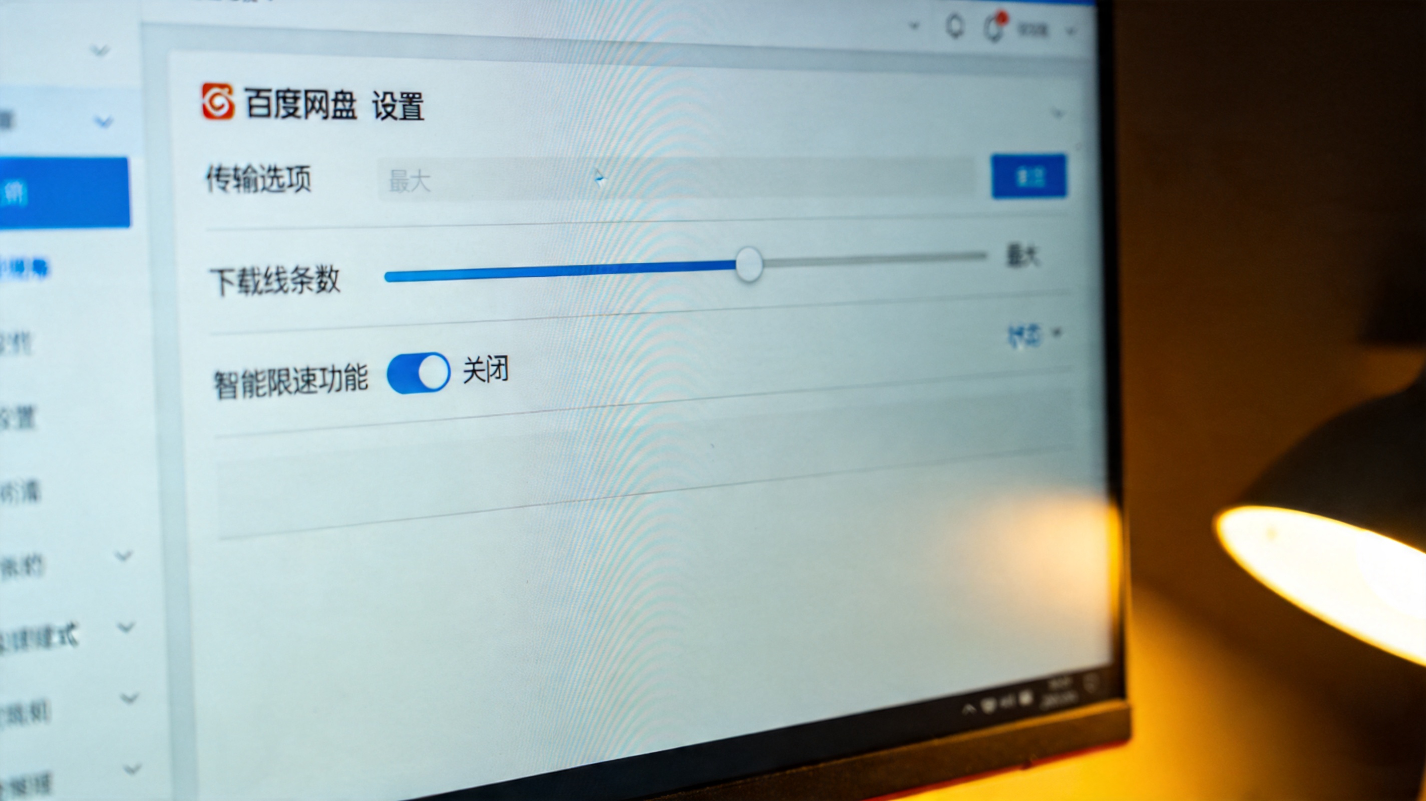 电脑屏幕显示百度网盘设置页面的传输选项，下载线程数调至最大，智能限速功能处于关闭状态，桌面角落有台灯暖光