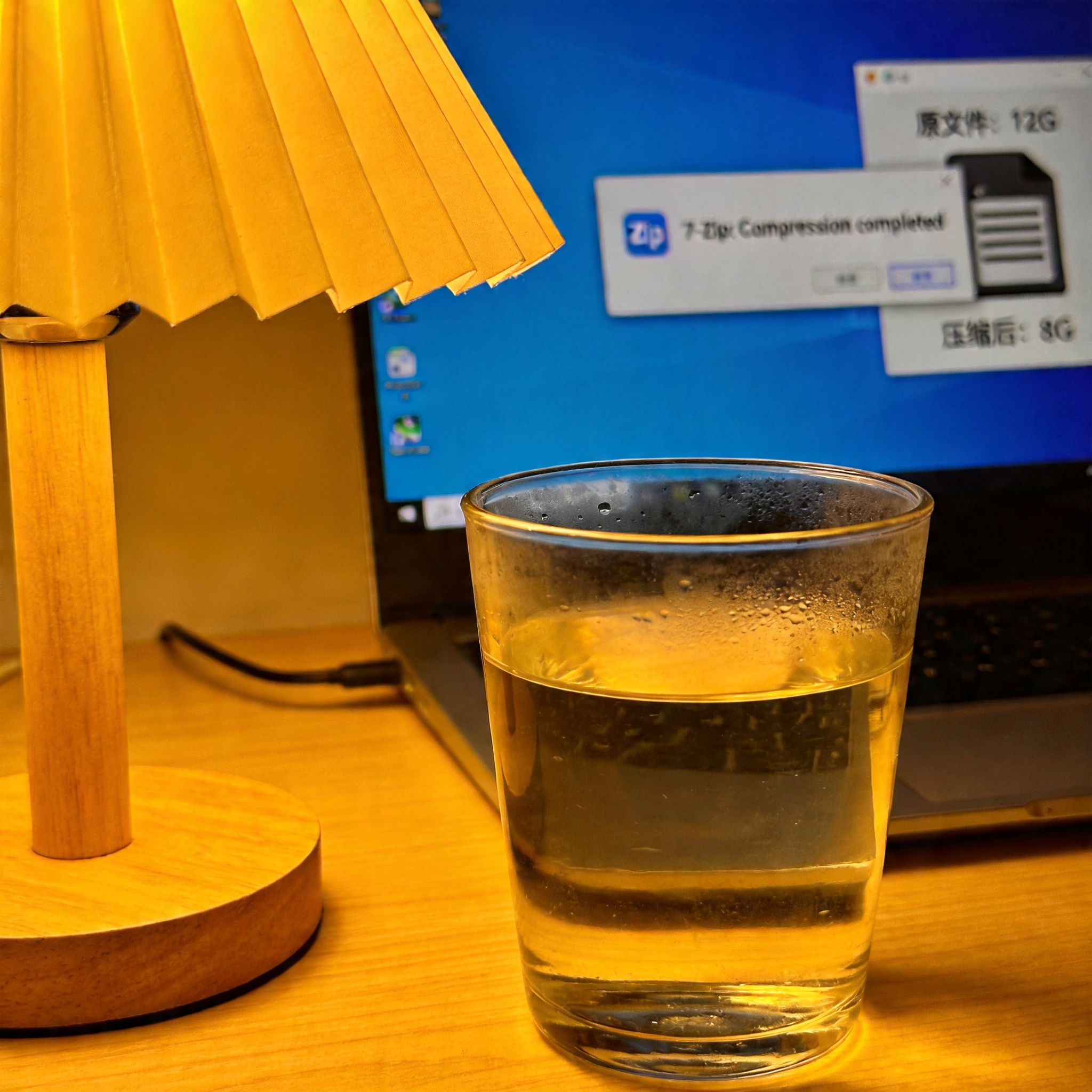电脑屏幕显示7Zip压缩完成提示框，旁边的硬盘图标显示原文件12G、压缩后8G，桌面角落放着半杯温水，台灯暖光