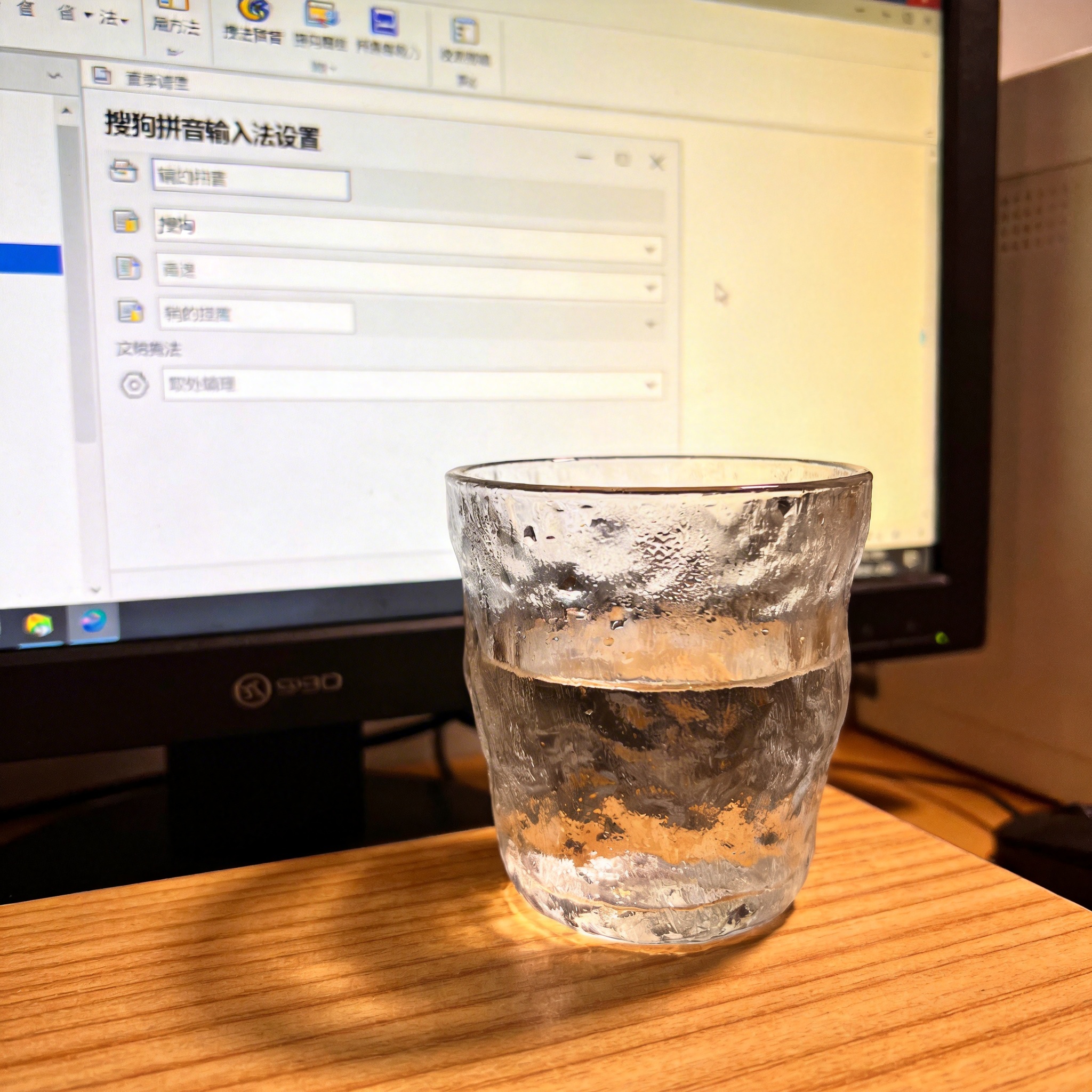 书桌上的主机，屏幕显示搜狗拼音设置界面，桌角放着水杯，自然光