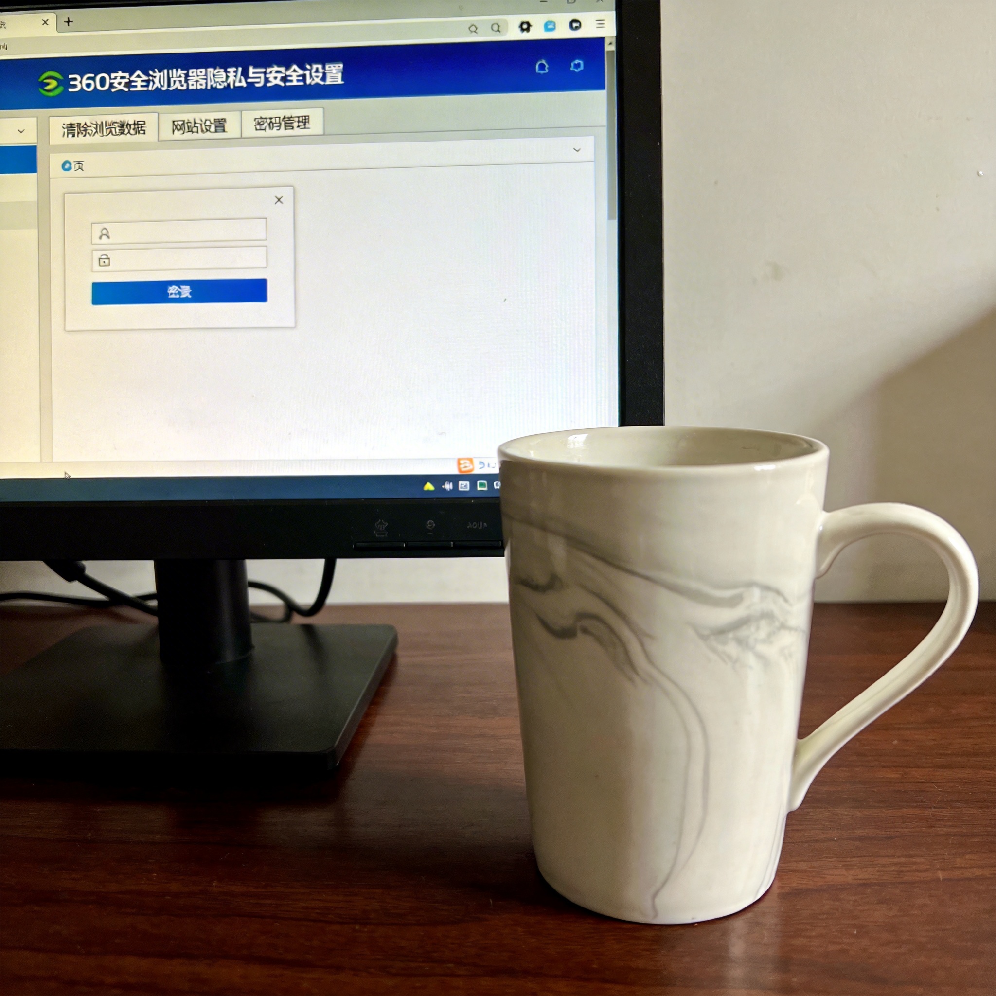 电脑桌前的电脑，屏幕显示360安全浏览器的隐私与安全设置界面，旁边放着陶瓷水杯，室内自然光