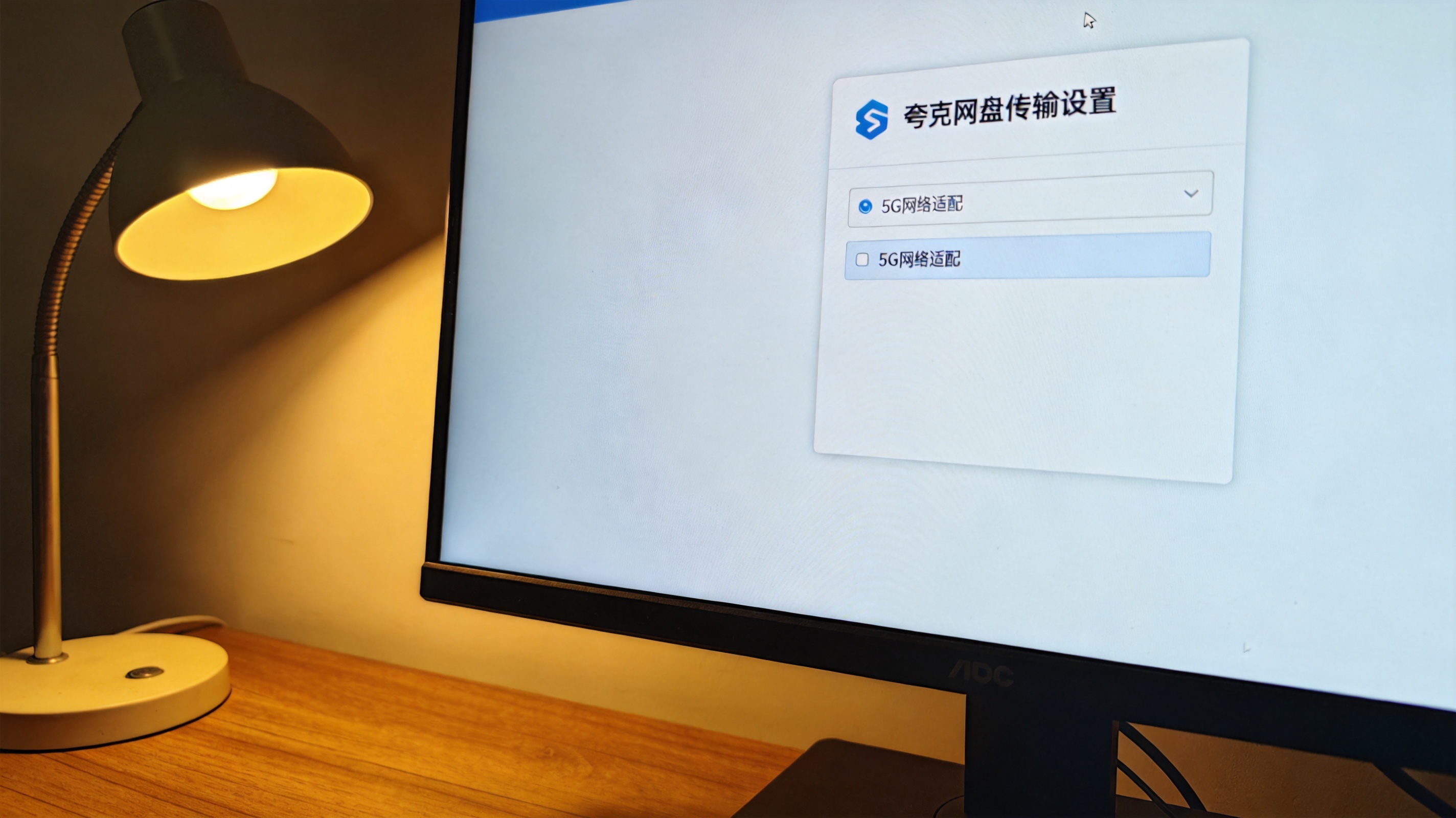 电脑屏幕显示夸克网盘传输设置界面，界面上有5G网络适配选项，桌面角落摆着台灯，屏幕光照亮桌面局部