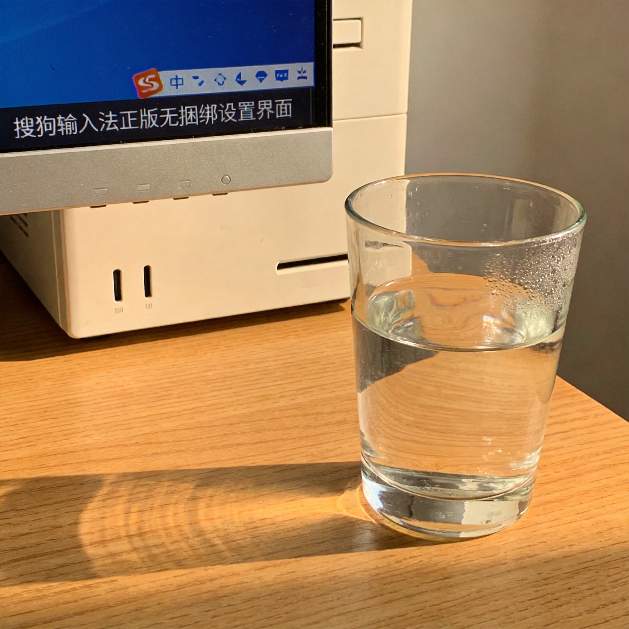 书桌上的主机，屏幕显示搜狗输入法正版无捆绑设置界面，桌角放着水杯，自然光
