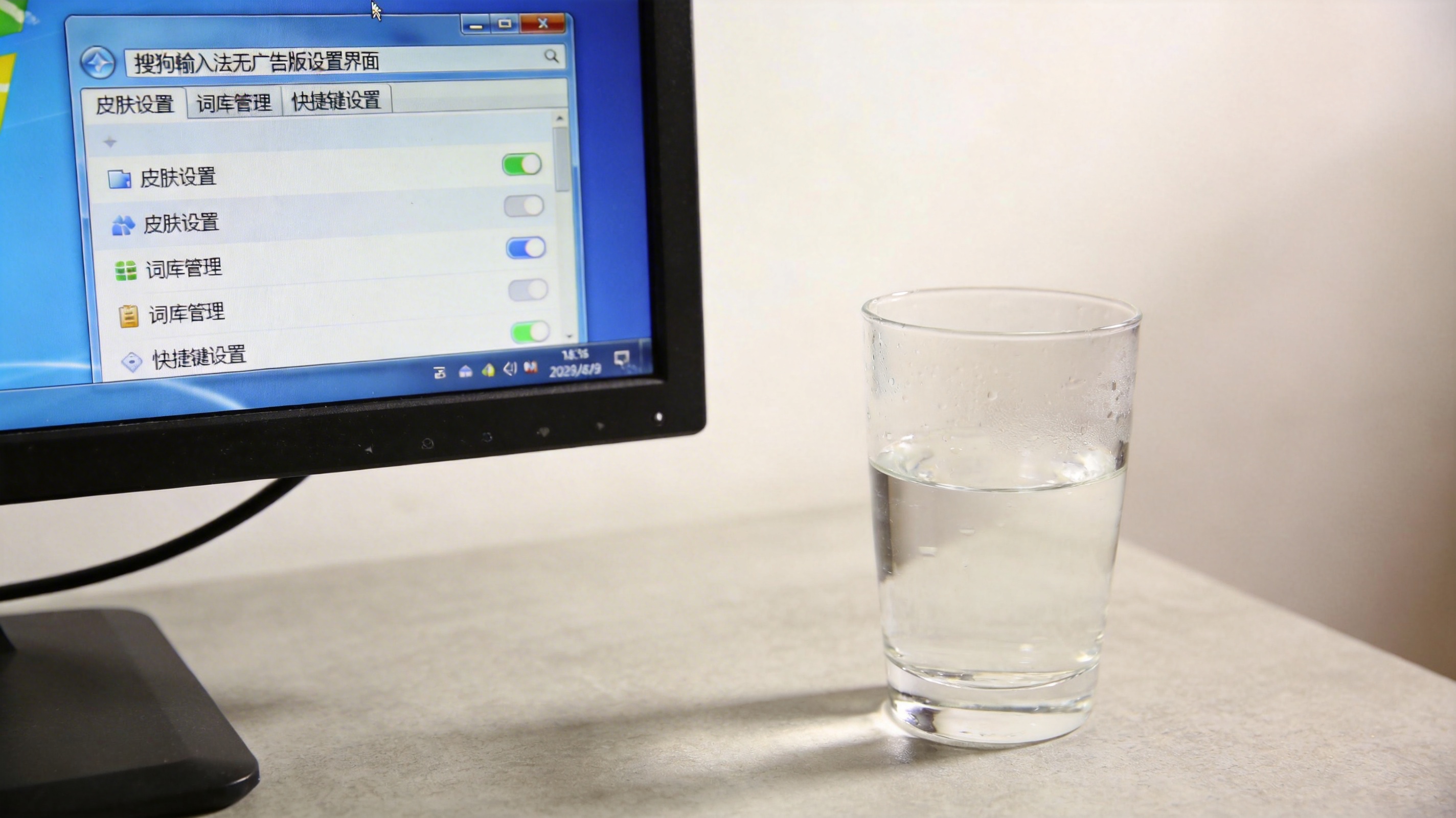 电脑桌面，屏幕显示Windows系统下的搜狗输入法无广告版设置界面，旁边放着半杯凉白开，室内自然光