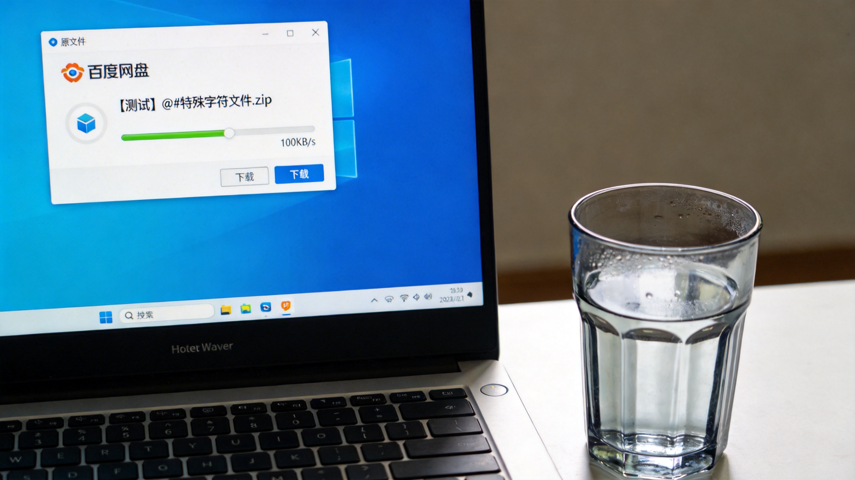 电脑桌面，屏幕显示百度网盘客户端下载界面，原文件名带特殊字符，下载速度显示100KB，旁边放着半透明水杯，室内自然光