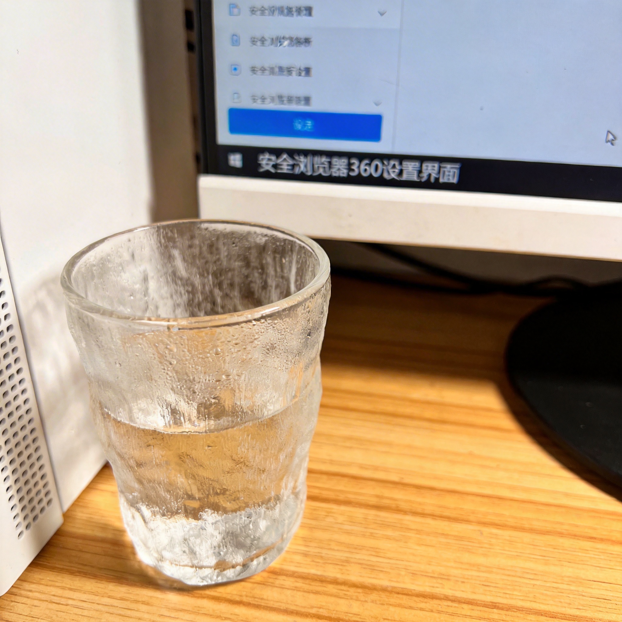 书桌上的主机，屏幕显示安全浏览器 360设置界面，桌角放着水杯，自然光
