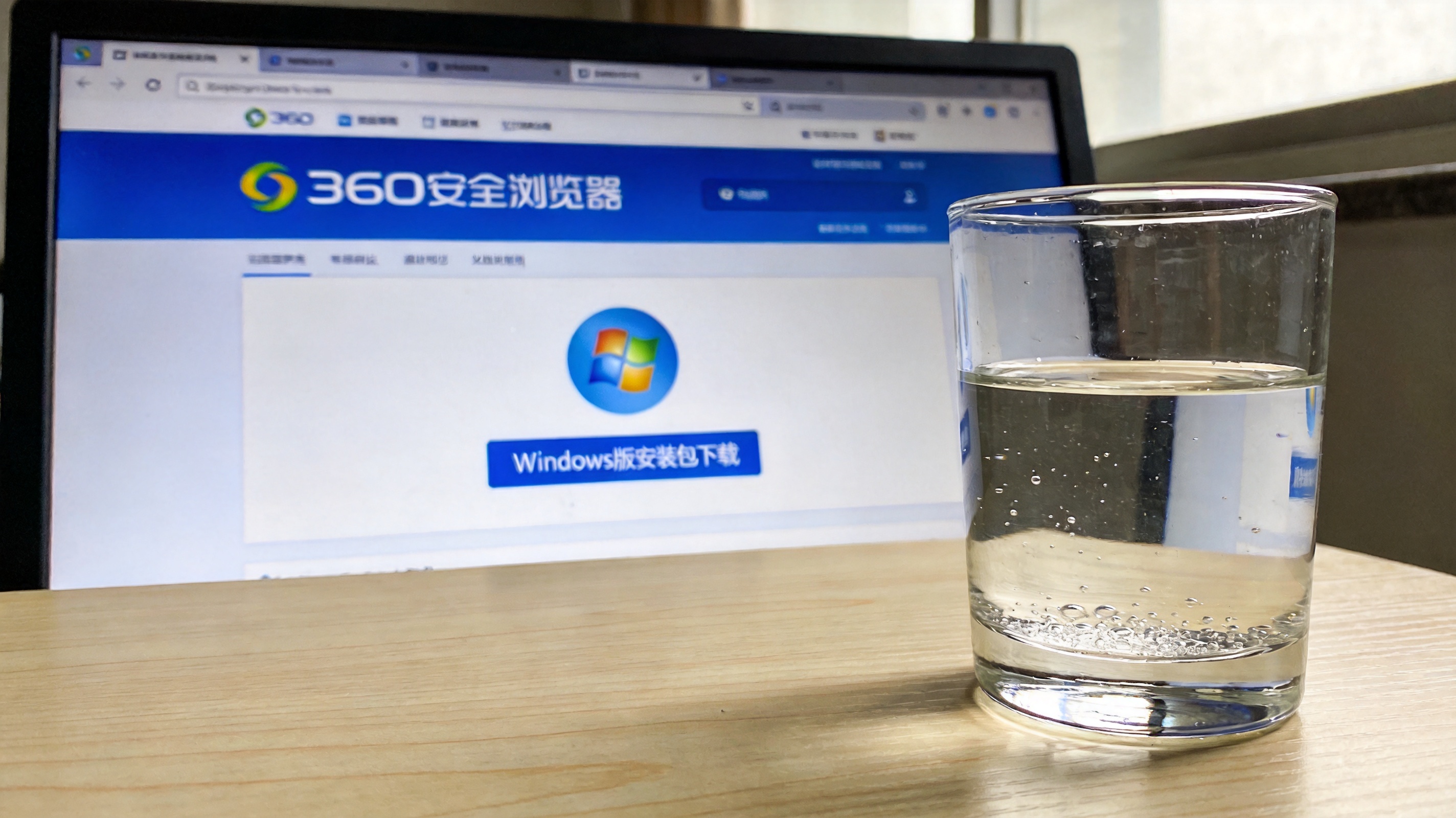 电脑桌面显示360安全浏览器官网页面，页面上有Windows版安装包下载按钮，桌面旁放着半杯凉白开，室内自然光