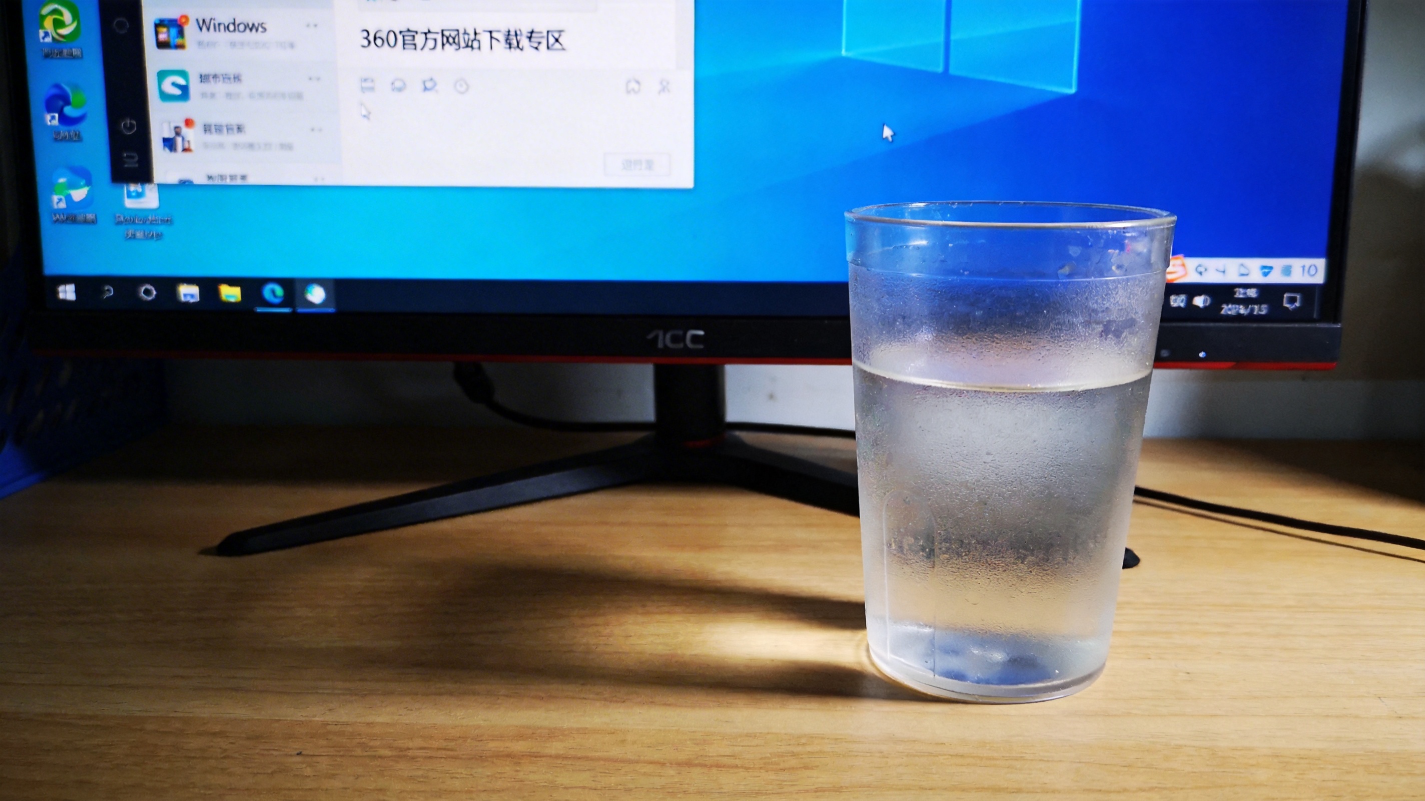 电脑桌面，屏幕显示Windows10系统自带浏览器打开的360官方网站下载专区，旁边放着半透明水杯，室内自然光