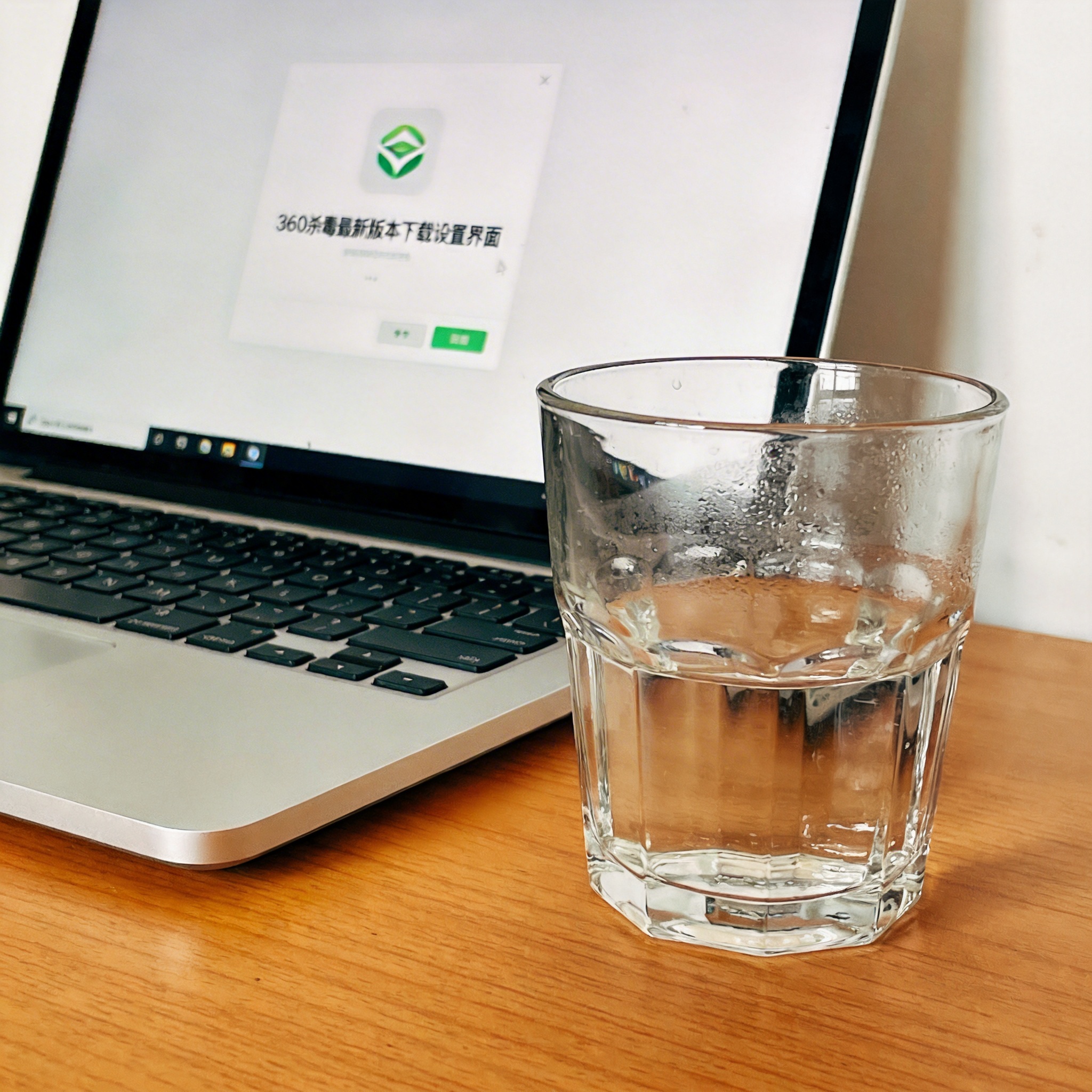 书桌上的笔记本，屏幕显示360 杀毒最新版本下载设置界面，桌角放着水杯，自然光