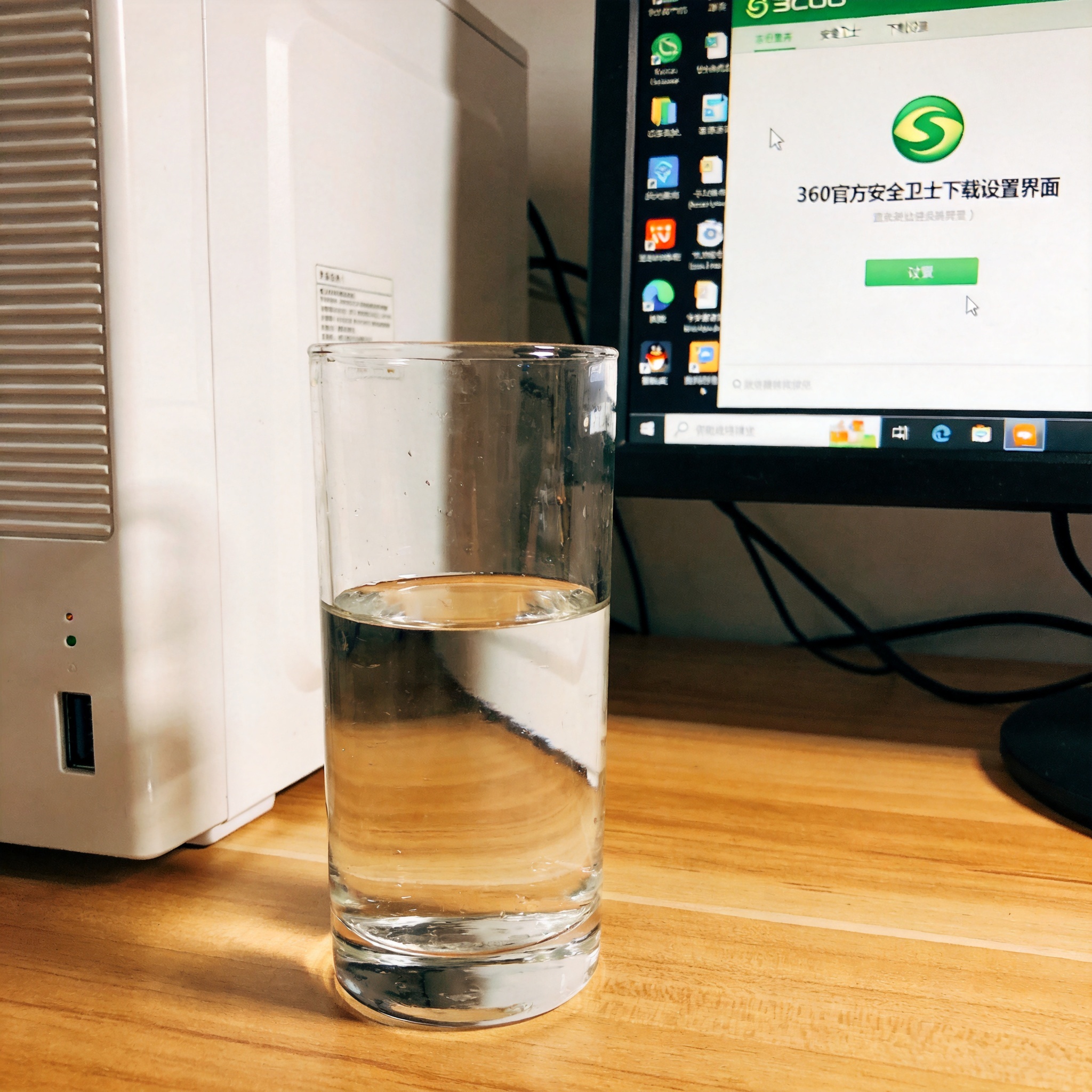 书桌上的主机，屏幕显示360 官方安全卫士下载设置界面，桌角放着水杯，自然光