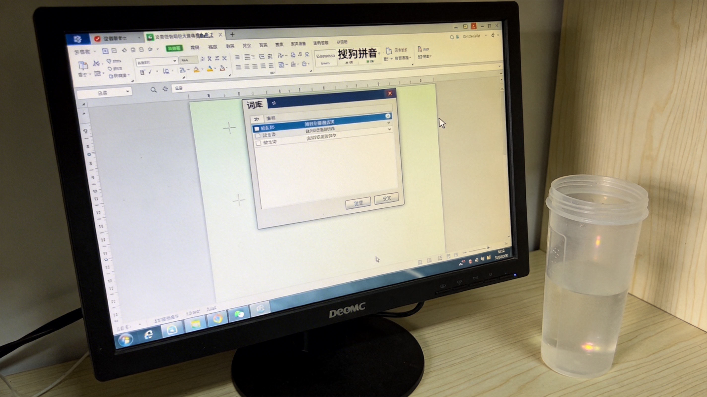 电脑桌面，屏幕显示搜狗拼音输入法的设置属性窗口，停在“词库”选项卡上，旁边放着半透明塑料水杯，室内自然光