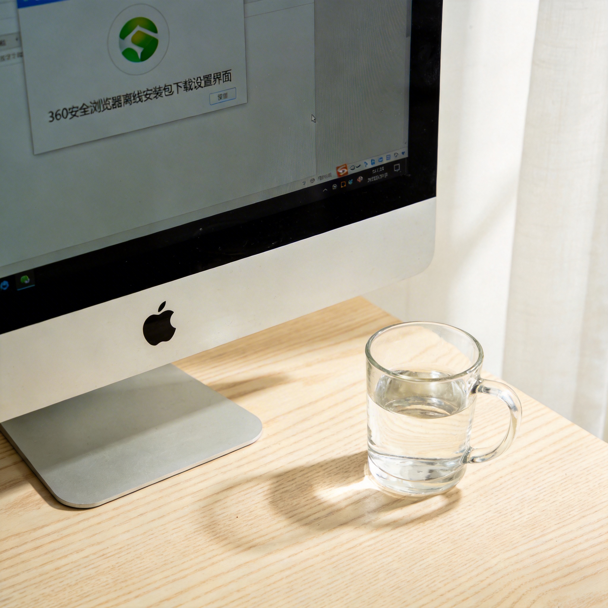 书桌上的电脑，屏幕显示360 安全浏览器离线安装包下载设置界面，桌角放着水杯，自然光