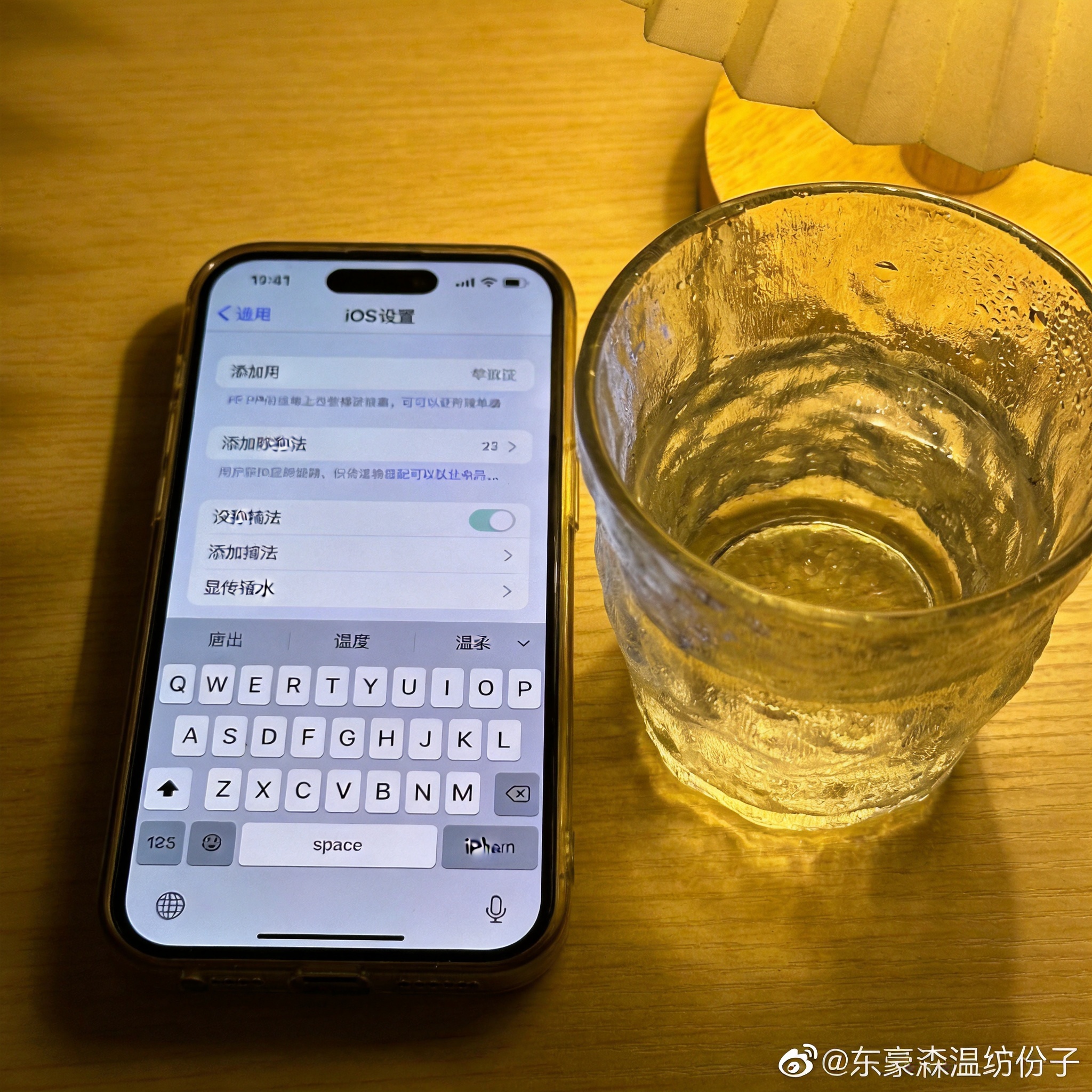 桌面放置的iPhone，屏幕显示iOS系统设置的键盘界面，已添加搜狗输入法，旁边放着半杯温水，台灯暖光