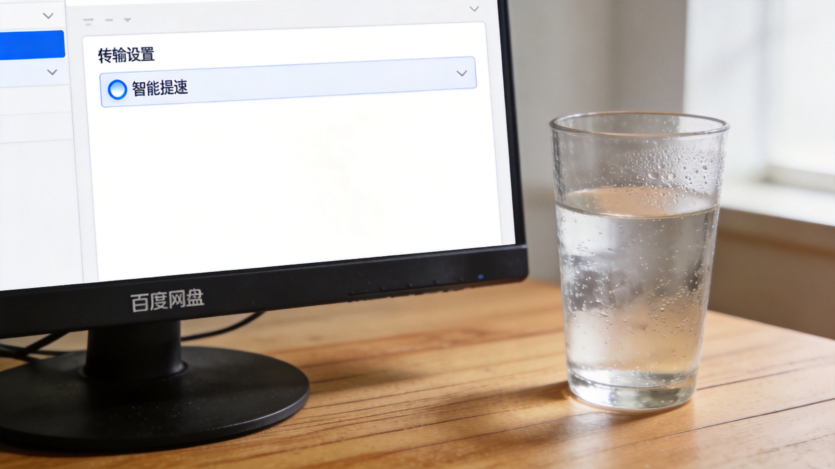 电脑桌面，屏幕显示百度网盘设置界面，传输设置栏里“智能提速”选项已勾选，旁边放着半杯凉水，室内自然光