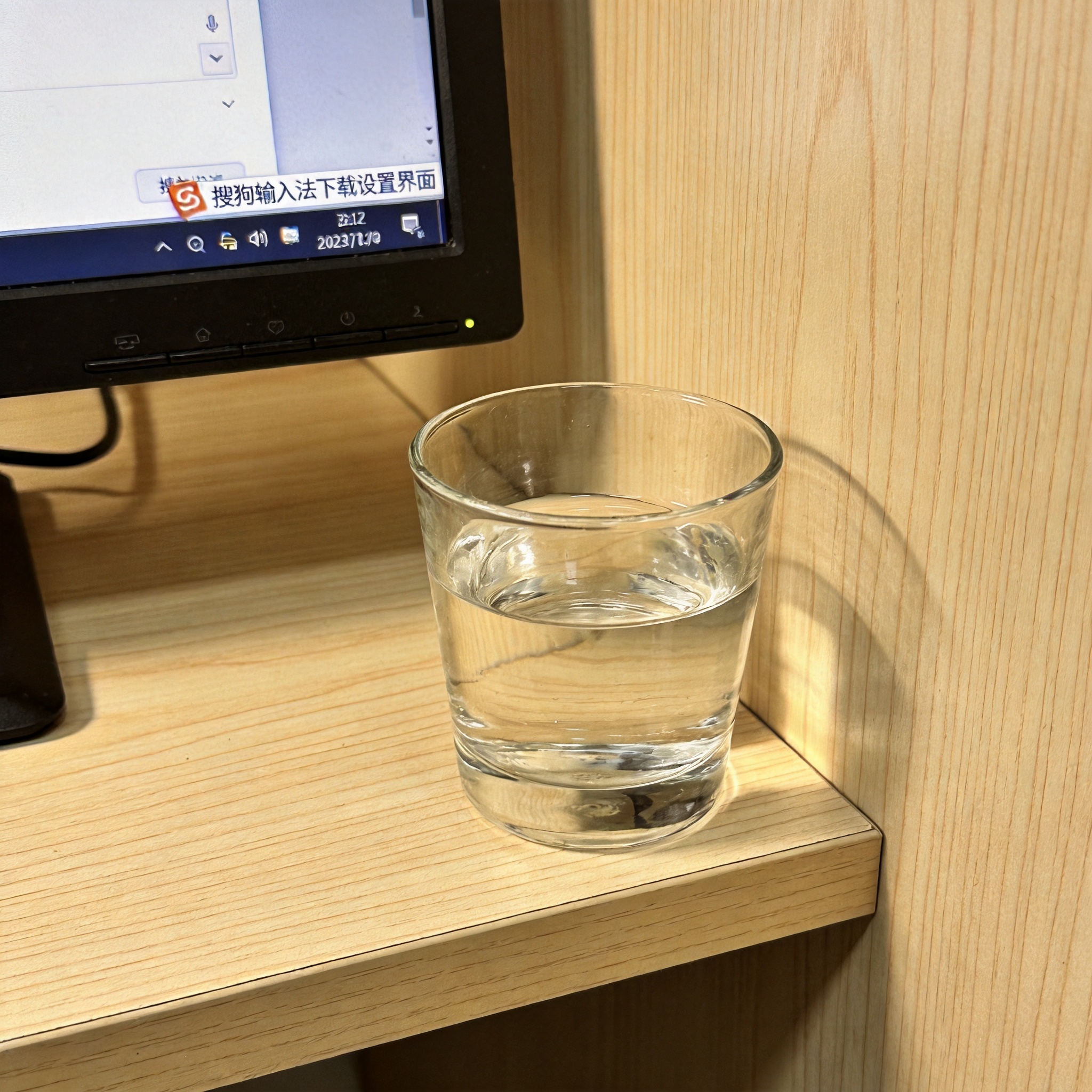 书桌上的电脑，屏幕显示搜狗输入法下载设置界面，桌角放着水杯，自然光