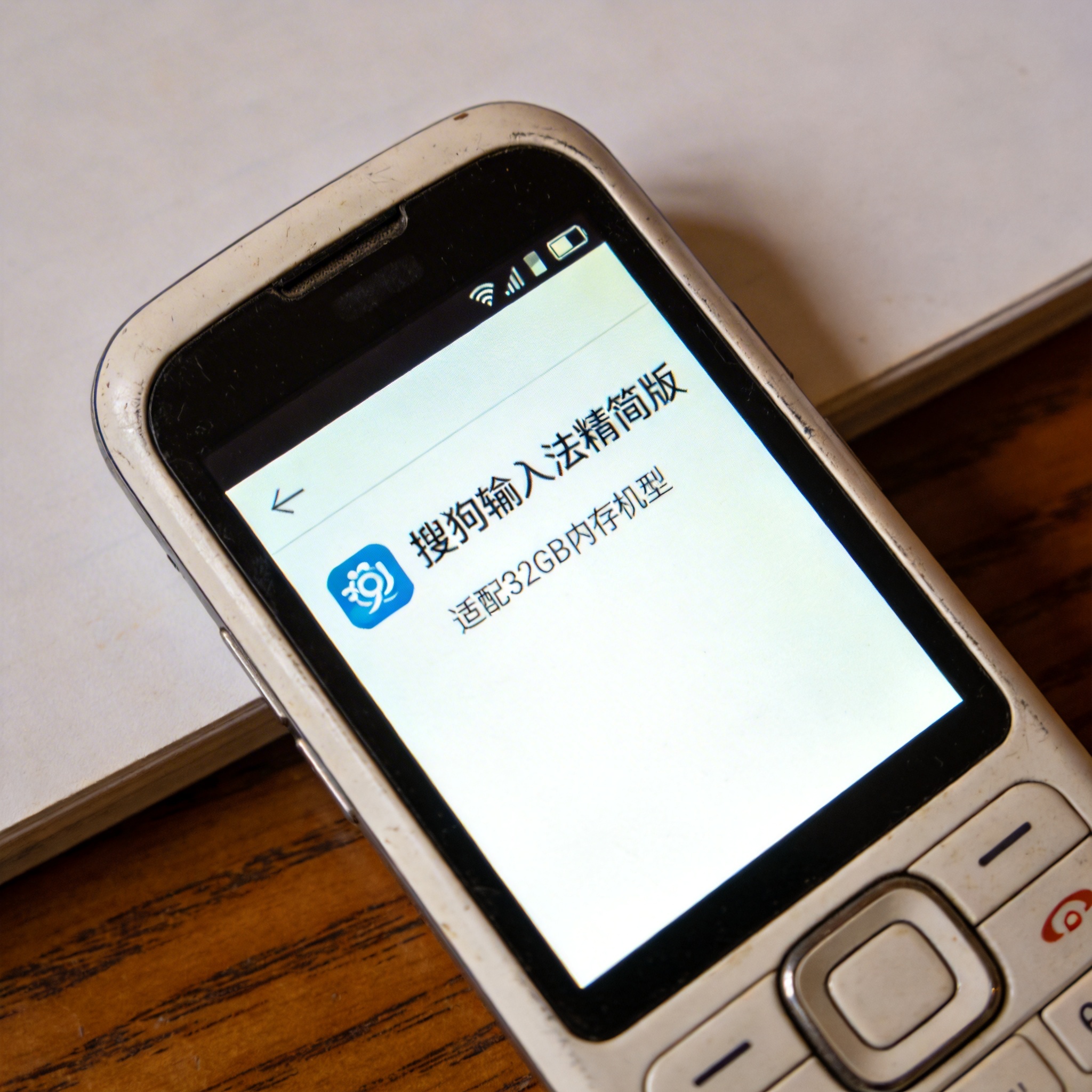 桌面的旧款智能手机，屏幕显示搜狗输入法精简版下载页面，标注适配32GB内存机型，屏幕光照明