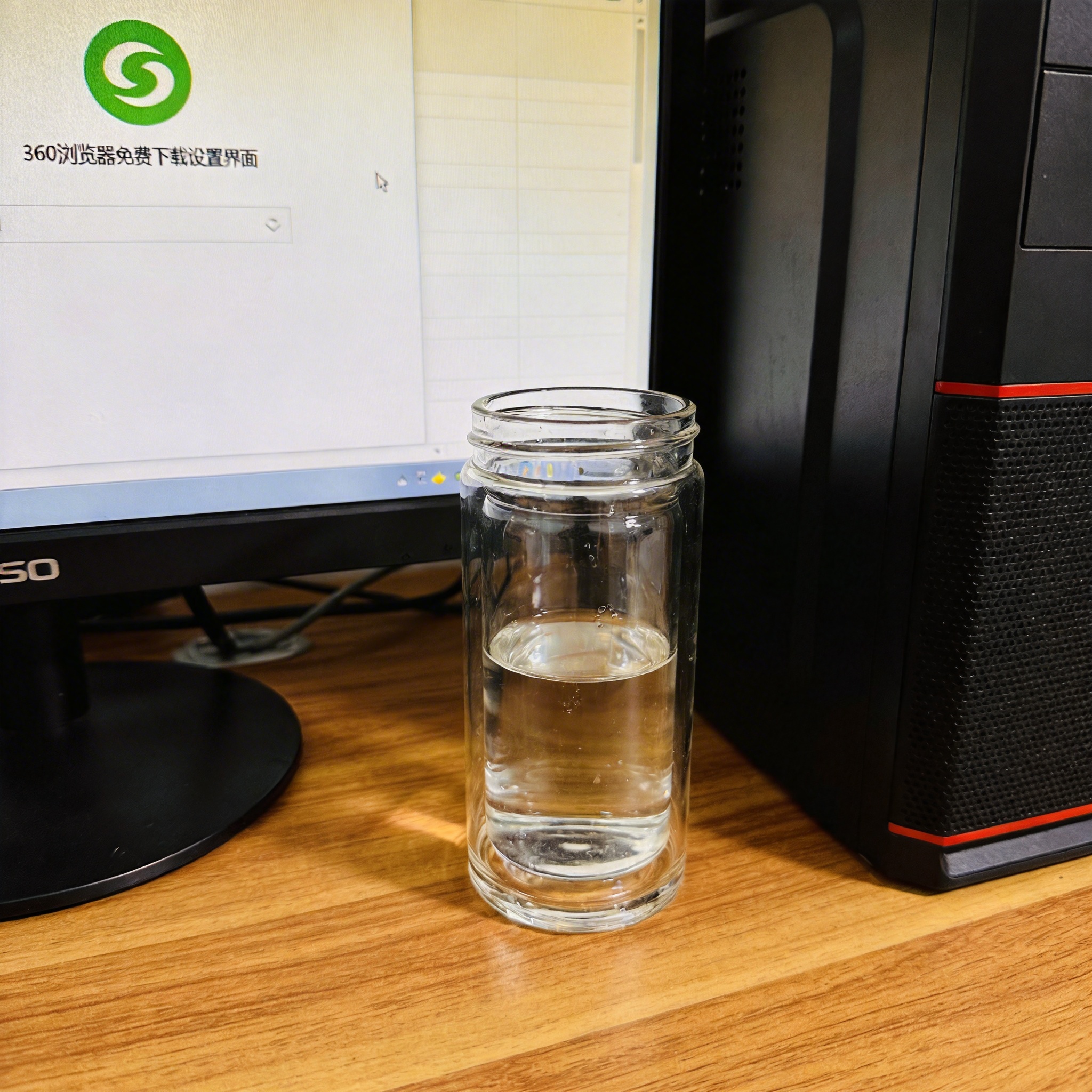 书桌上的主机，屏幕显示360 浏览器免费下载设置界面，桌角放着水杯，自然光