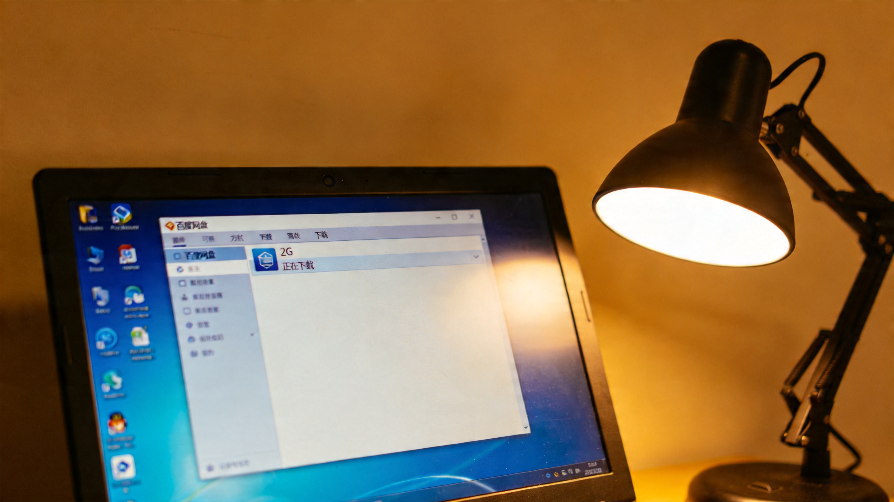 桌面上的Windows系统电脑，屏幕显示百度网盘下载列表，其中一个2G文件正在下载，旁边有打开的台灯