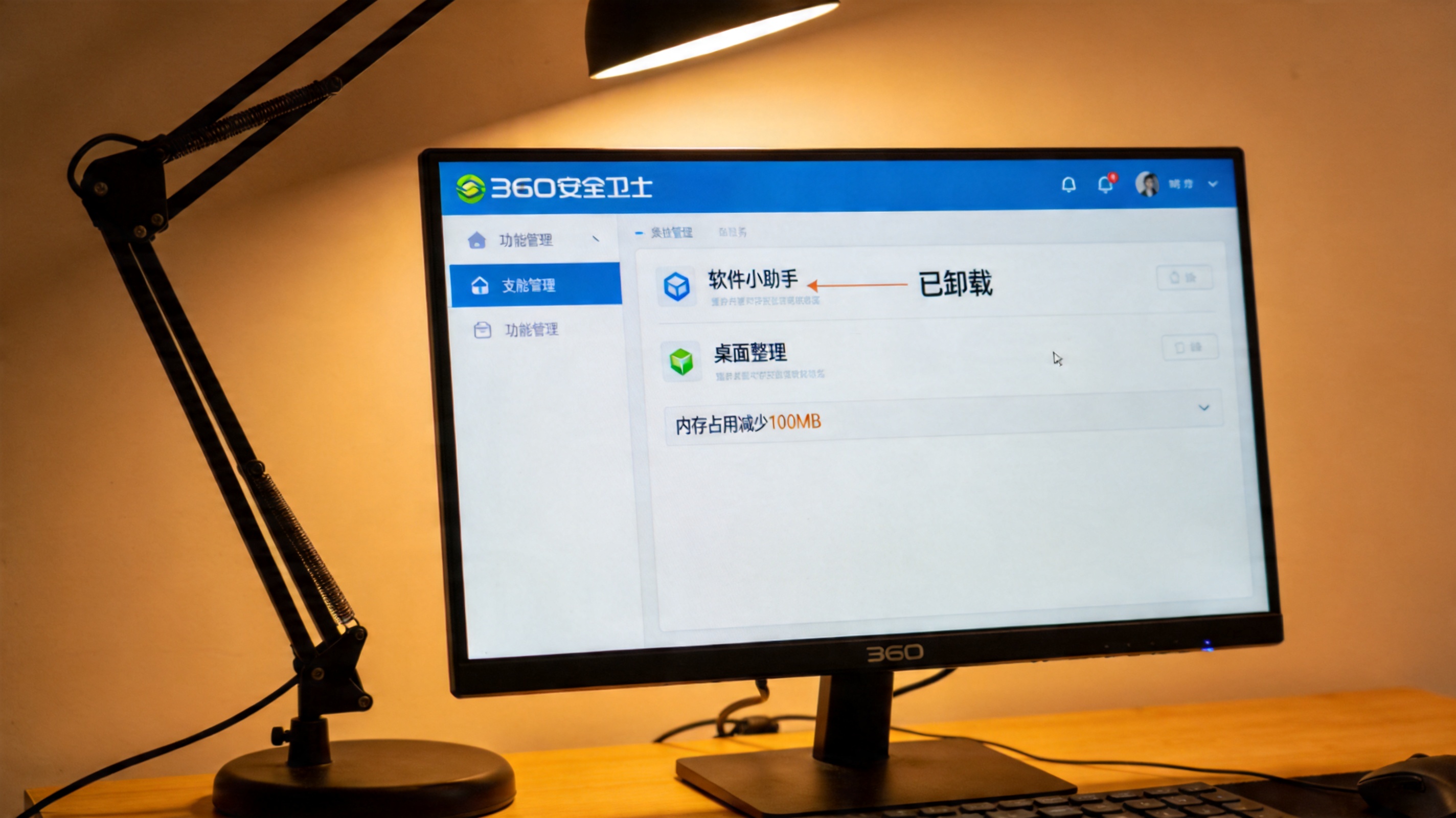 电脑屏幕显示360安全卫士功能管理界面，软件小助手、桌面整理选项旁标着已卸载，下方显示内存占用减少100MB，桌面角落有台台灯