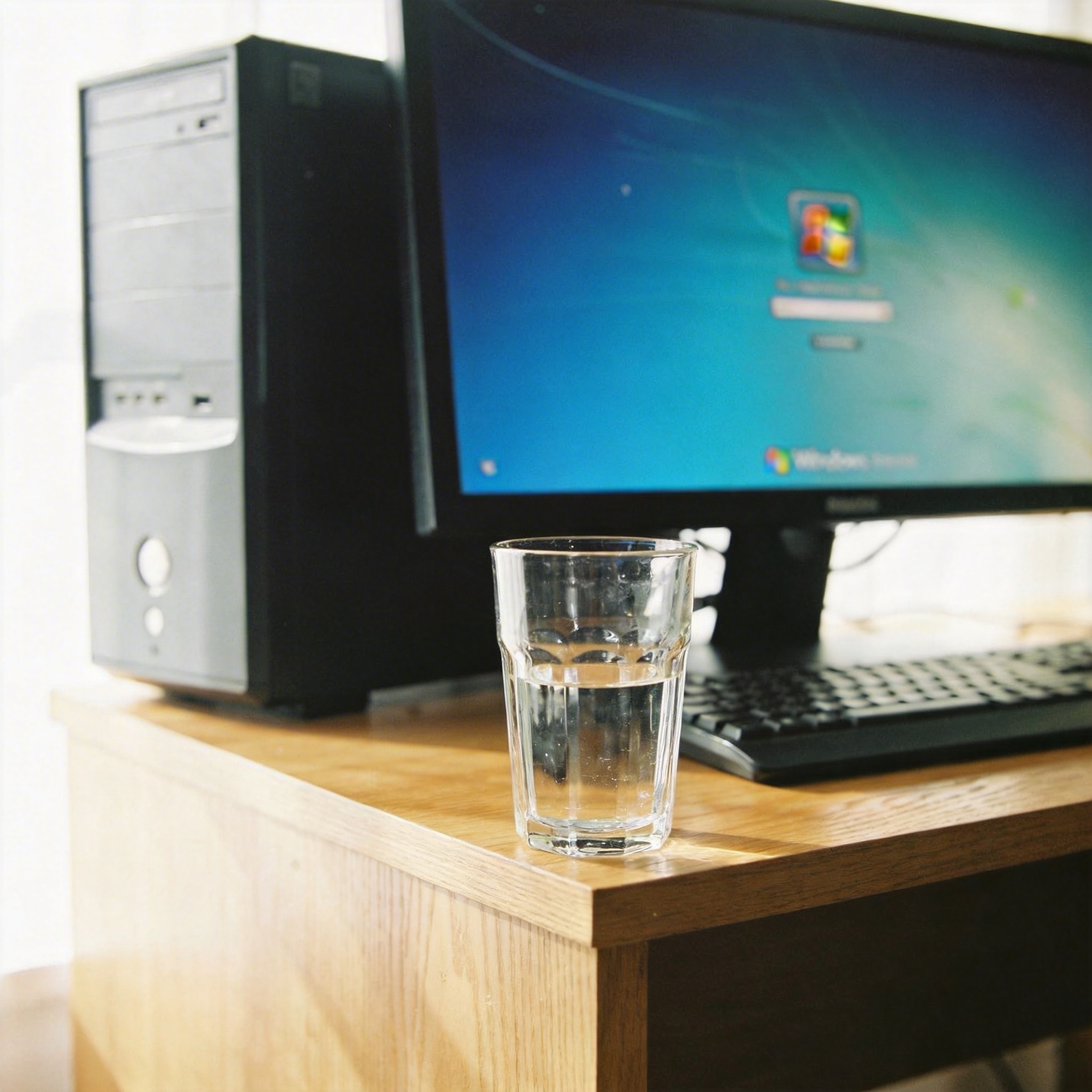 书桌上的主机，屏幕显示Windows设置界面，桌角放着水杯，自然光