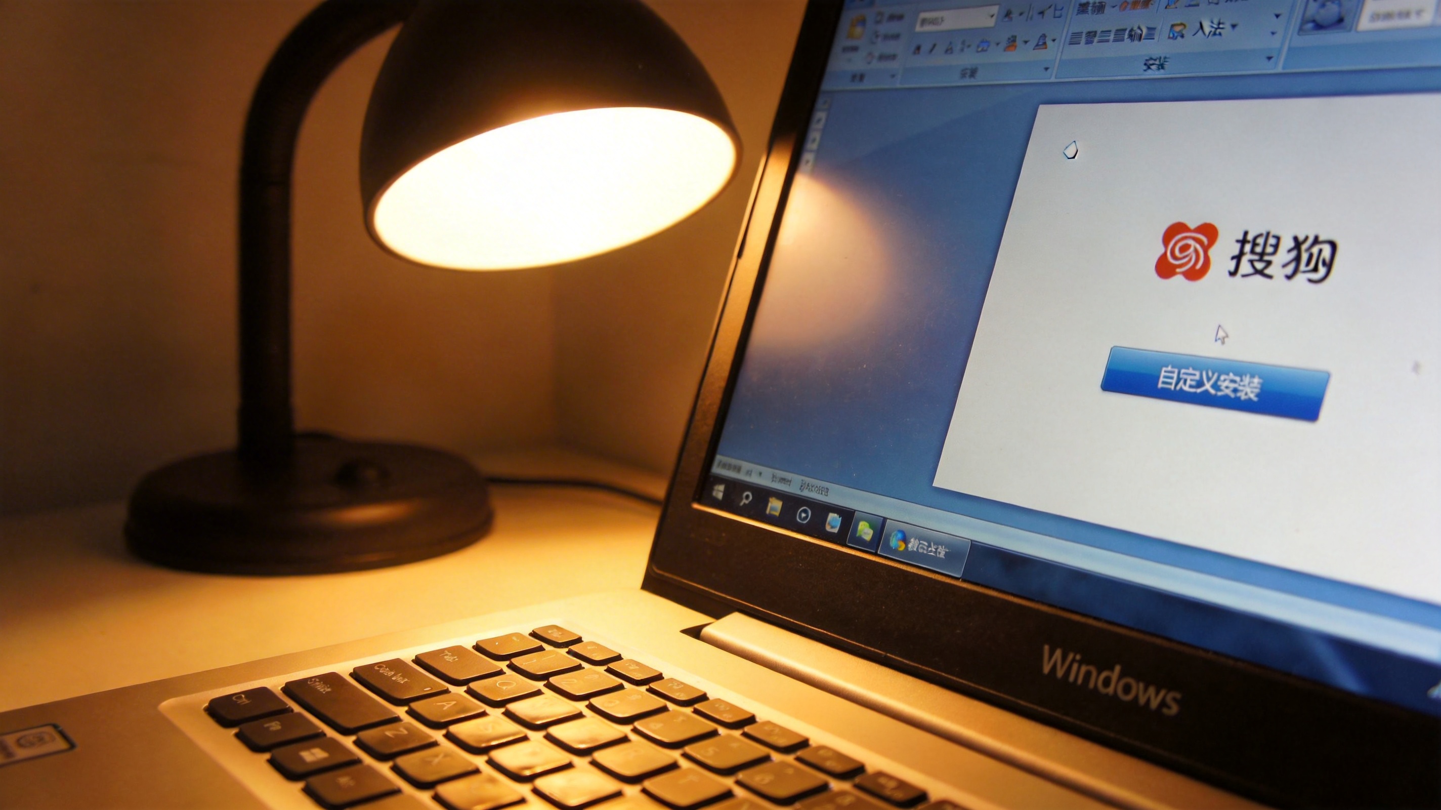 桌面的Windows系统电脑，屏幕显示搜狗输入法安装界面，界面上有自定义安装选项，台灯暖光落在键盘边缘