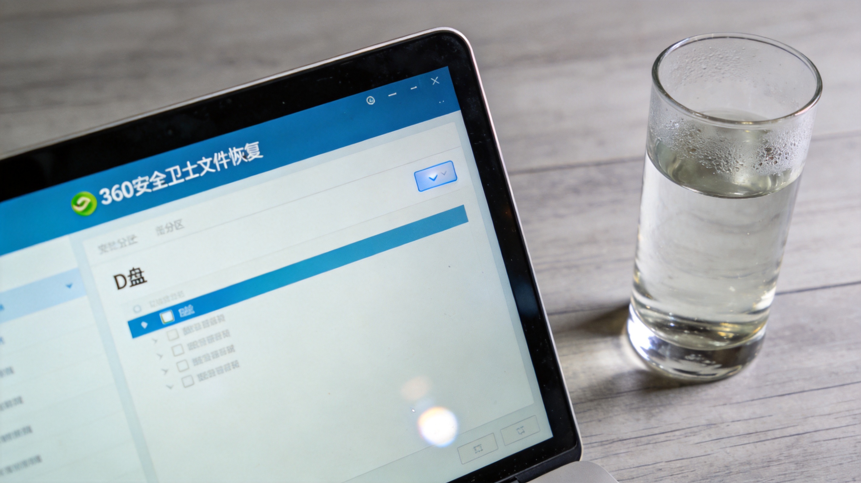 电脑桌面，屏幕显示360安全卫士文件恢复界面，选中D盘分区，旁边放着半杯温水，室内自然光