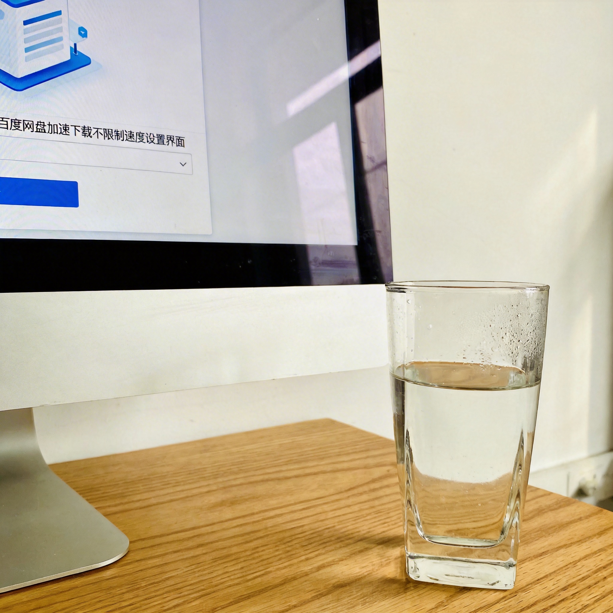 书桌上的主机，屏幕显示百度网盘加速下载不限制速度设置界面，桌角放着水杯，自然光