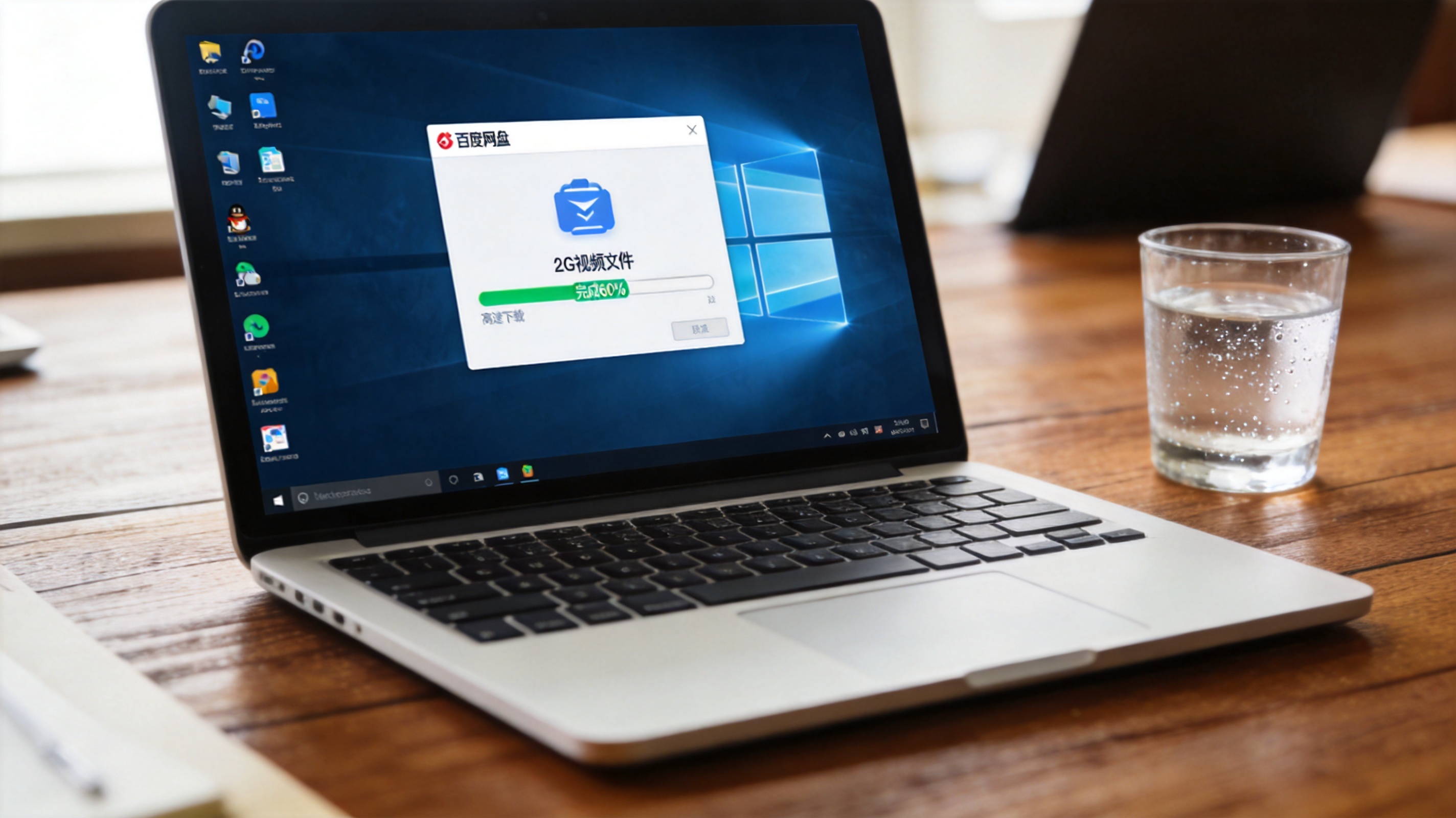 Windows系统的电脑放在桌面上，屏幕显示百度网盘下载界面，2G视频文件正在高速下载，进度条显示完成60%，桌面放着半杯温水