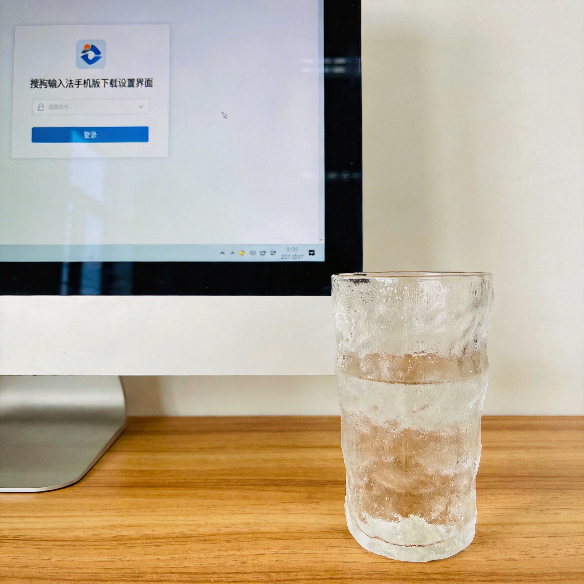 书桌上的主机，屏幕显示搜狗输入法手机版下载设置界面，桌角放着水杯，自然光