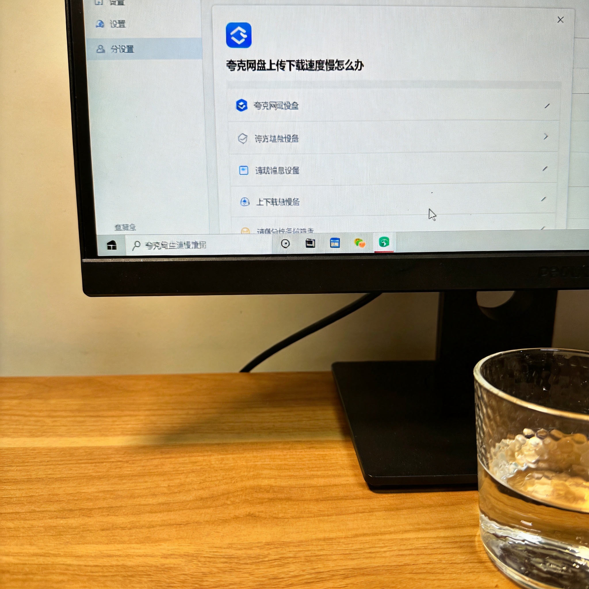 书桌上的主机，屏幕显示夸克网盘上传下载速度慢怎么办设置界面，桌角放着水杯，自然光