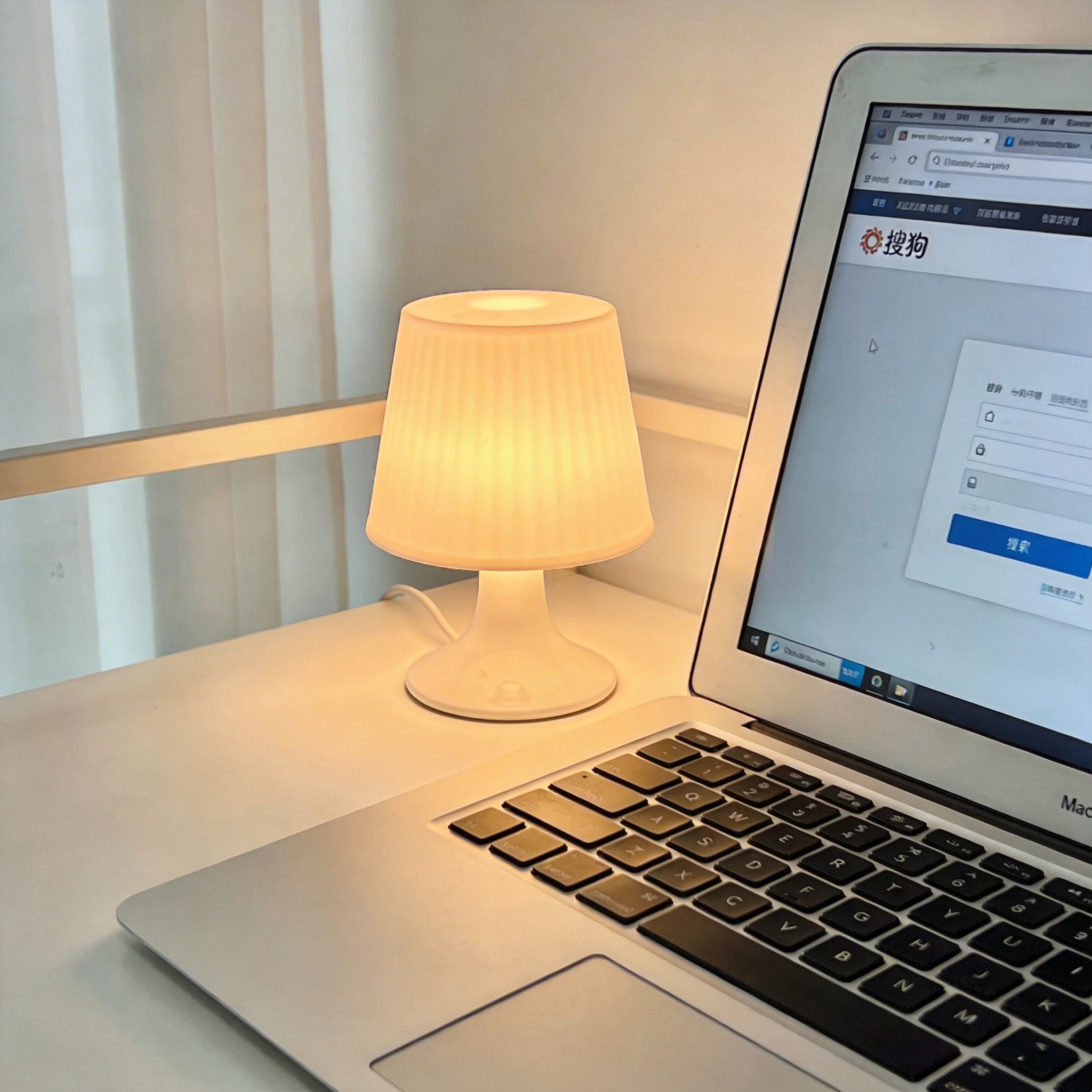 电脑桌上的电脑，屏幕显示搜狗界面，旁边放着台灯