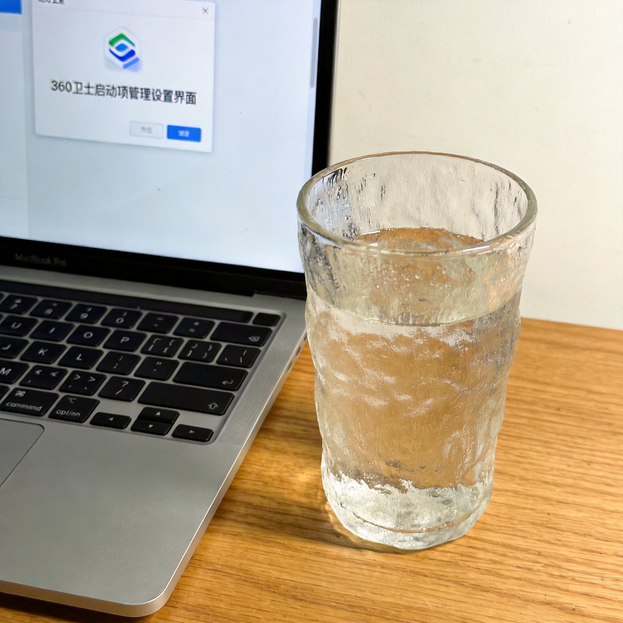 书桌上的笔记本，屏幕显示360 卫士启动项管理设置界面，桌角放着水杯，自然光