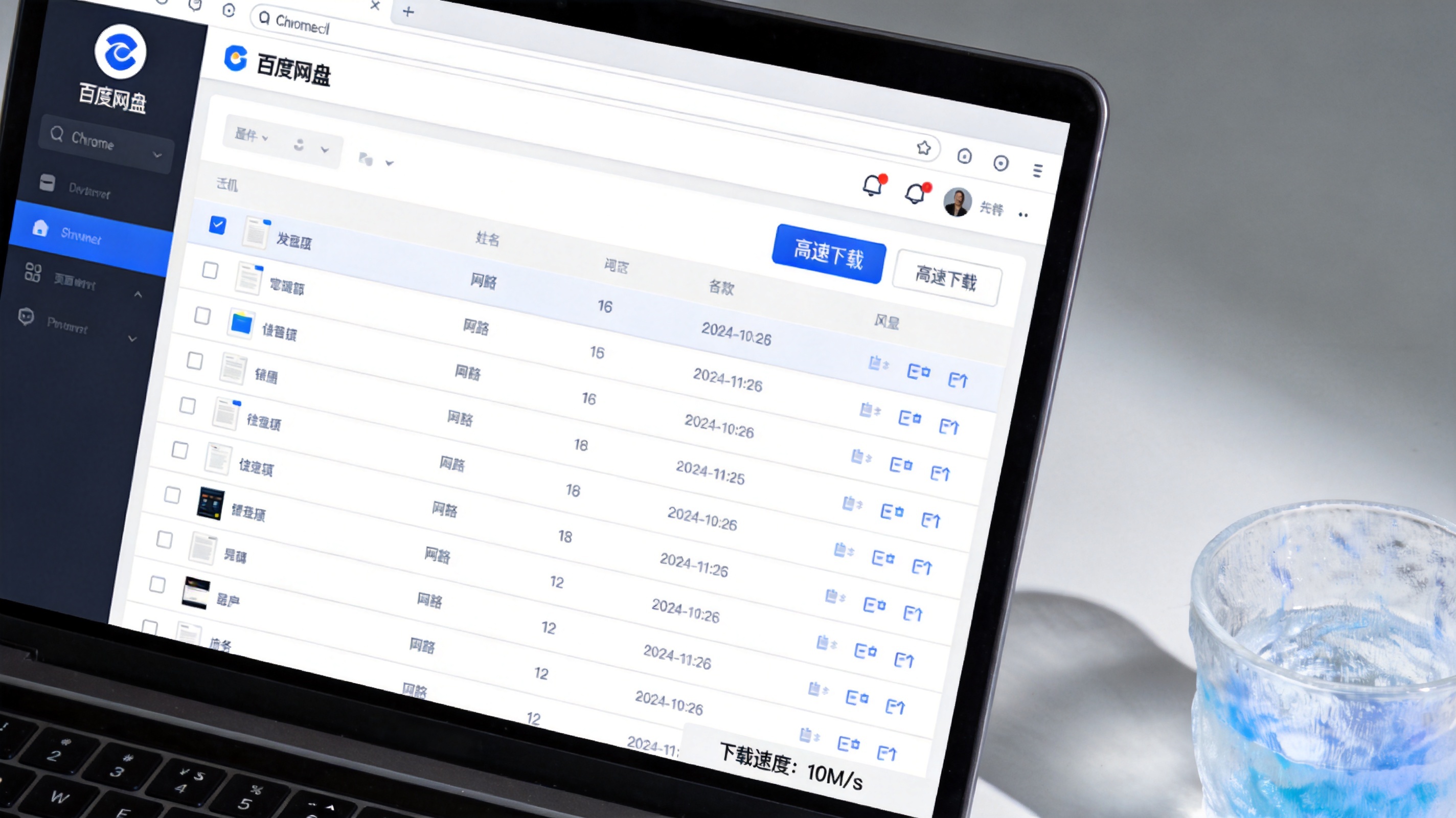 电脑桌面，Chrome浏览器打开百度网盘网页版，文件旁显示高速下载按钮，屏幕右下角显示下载速度每秒10M，桌面放着半透明塑料水杯