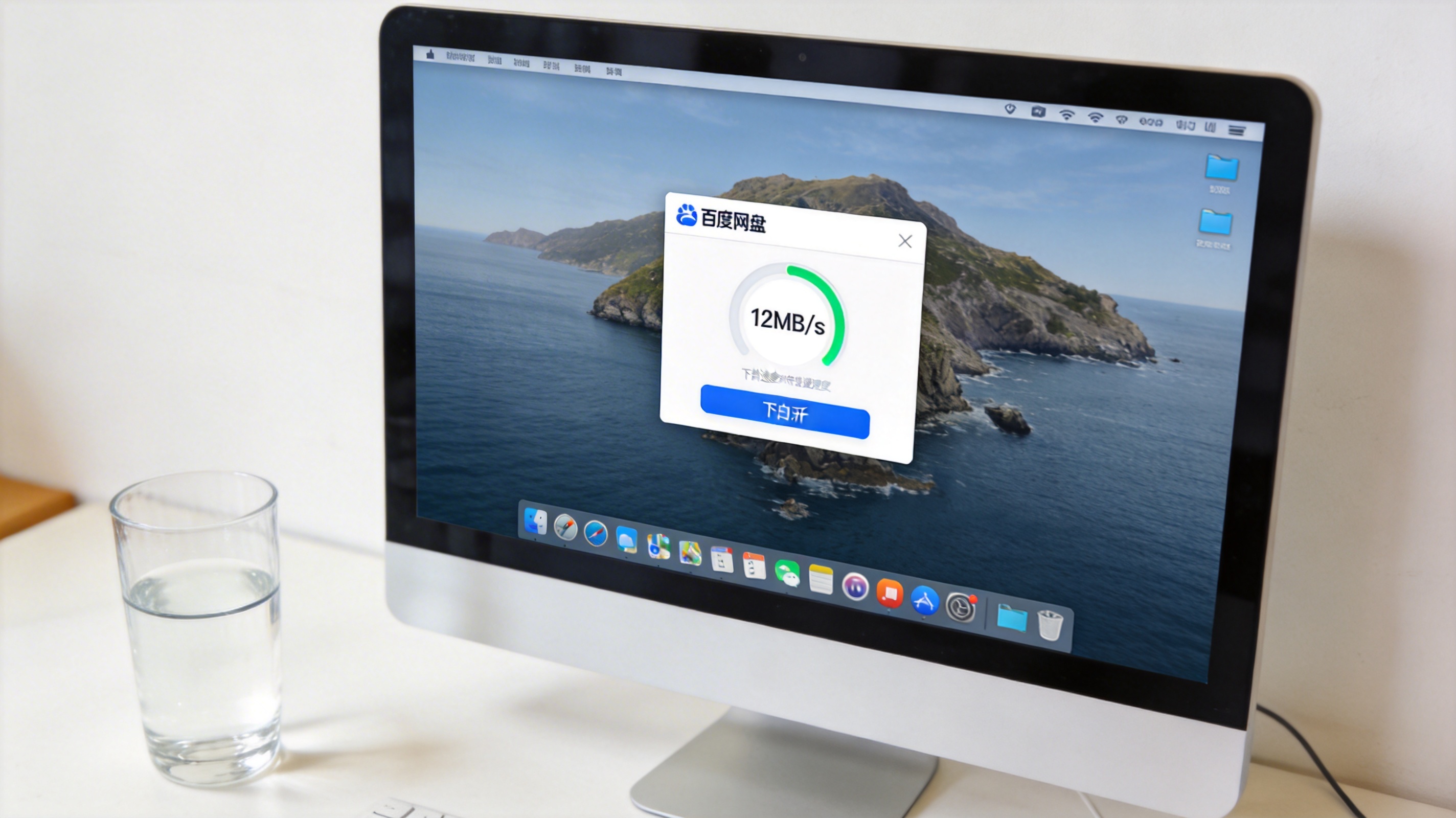 电脑桌面，屏幕显示百度网盘客户端界面，下载速度显示12MB/s，旁边放着半杯凉白开，室内自然光