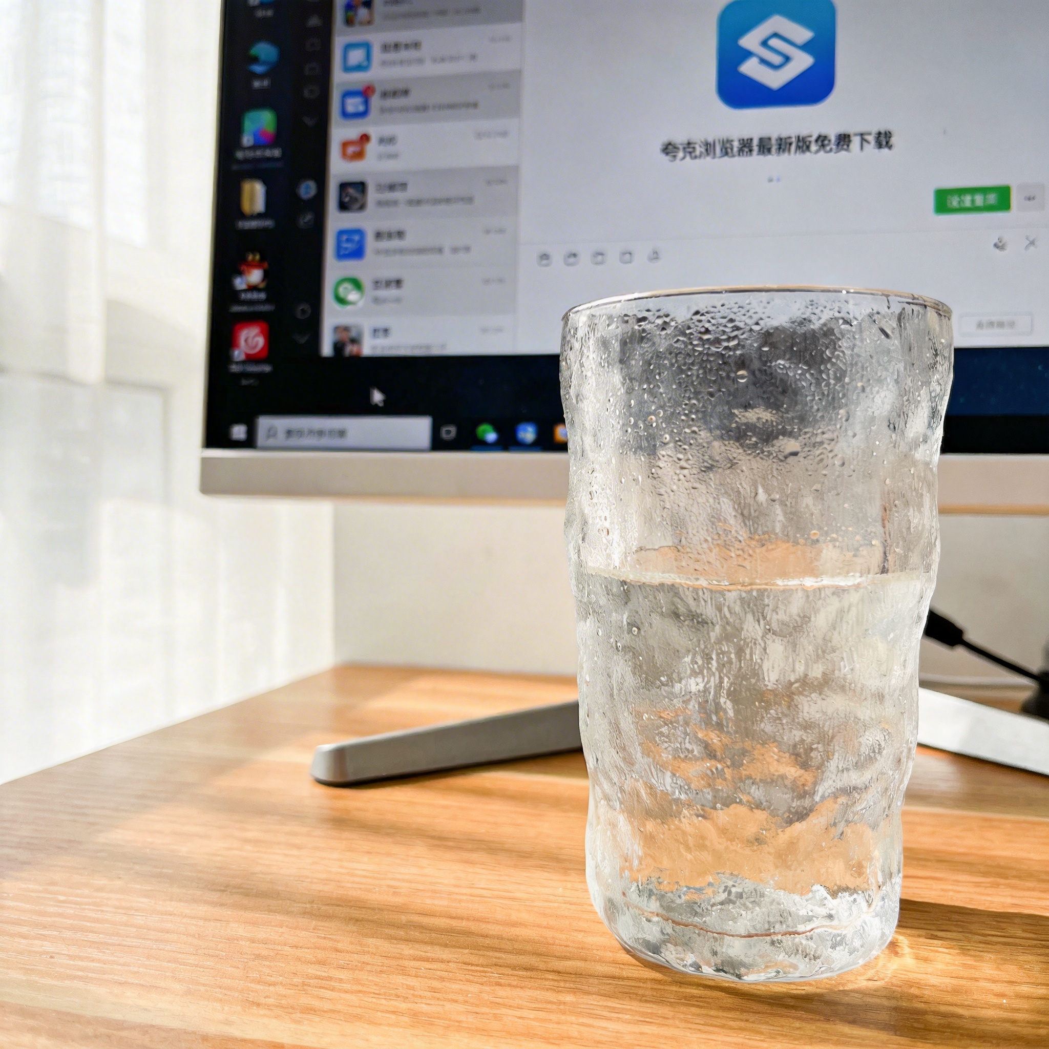 书桌上的主机，屏幕显示夸克浏览器最新版免费下载设置界面，桌角放着水杯，自然光