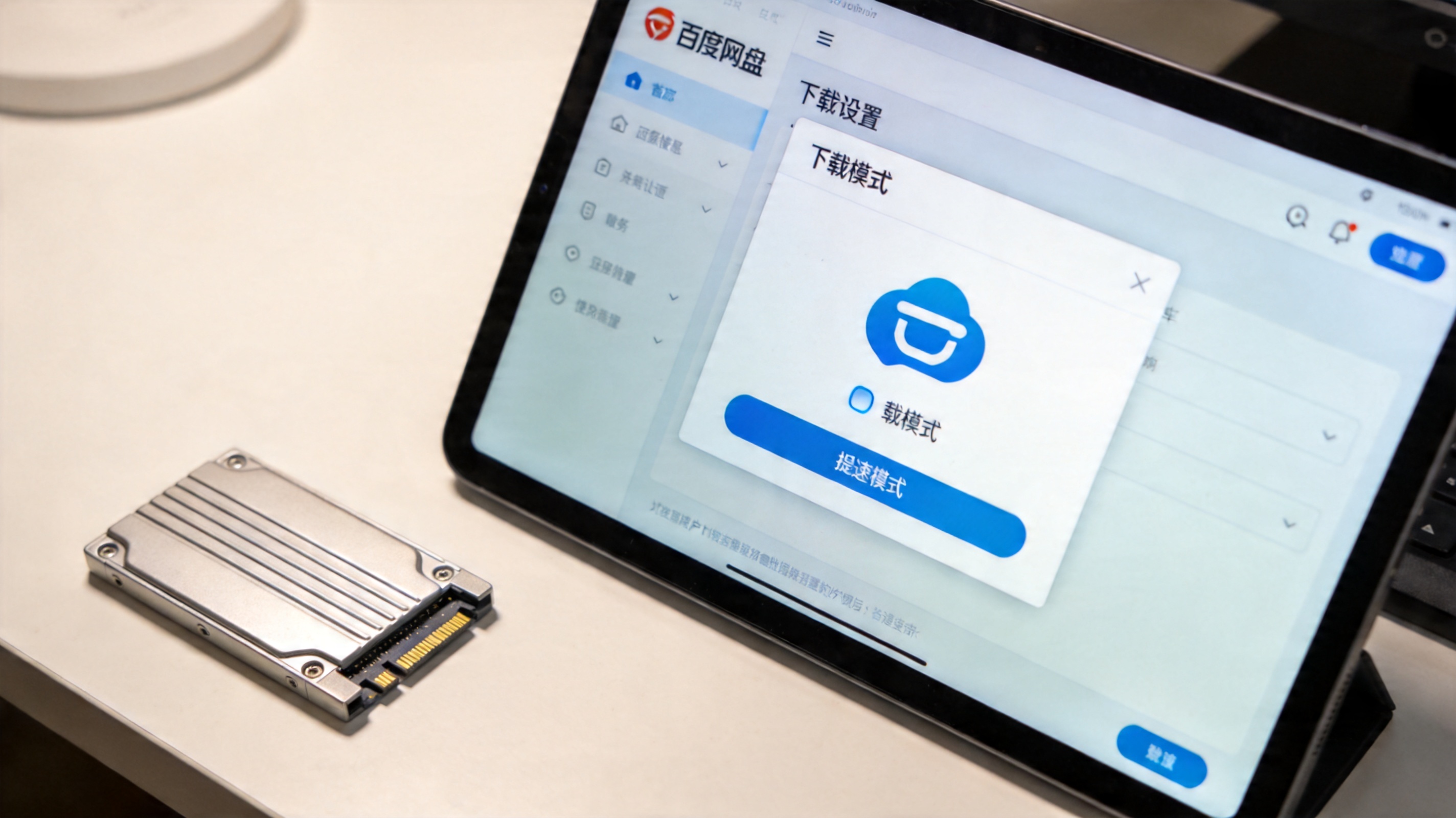 电脑桌面，屏幕显示百度网盘客户端的下载设置窗口，下载模式选为提速模式，旁边放着固态硬盘，室内自然光