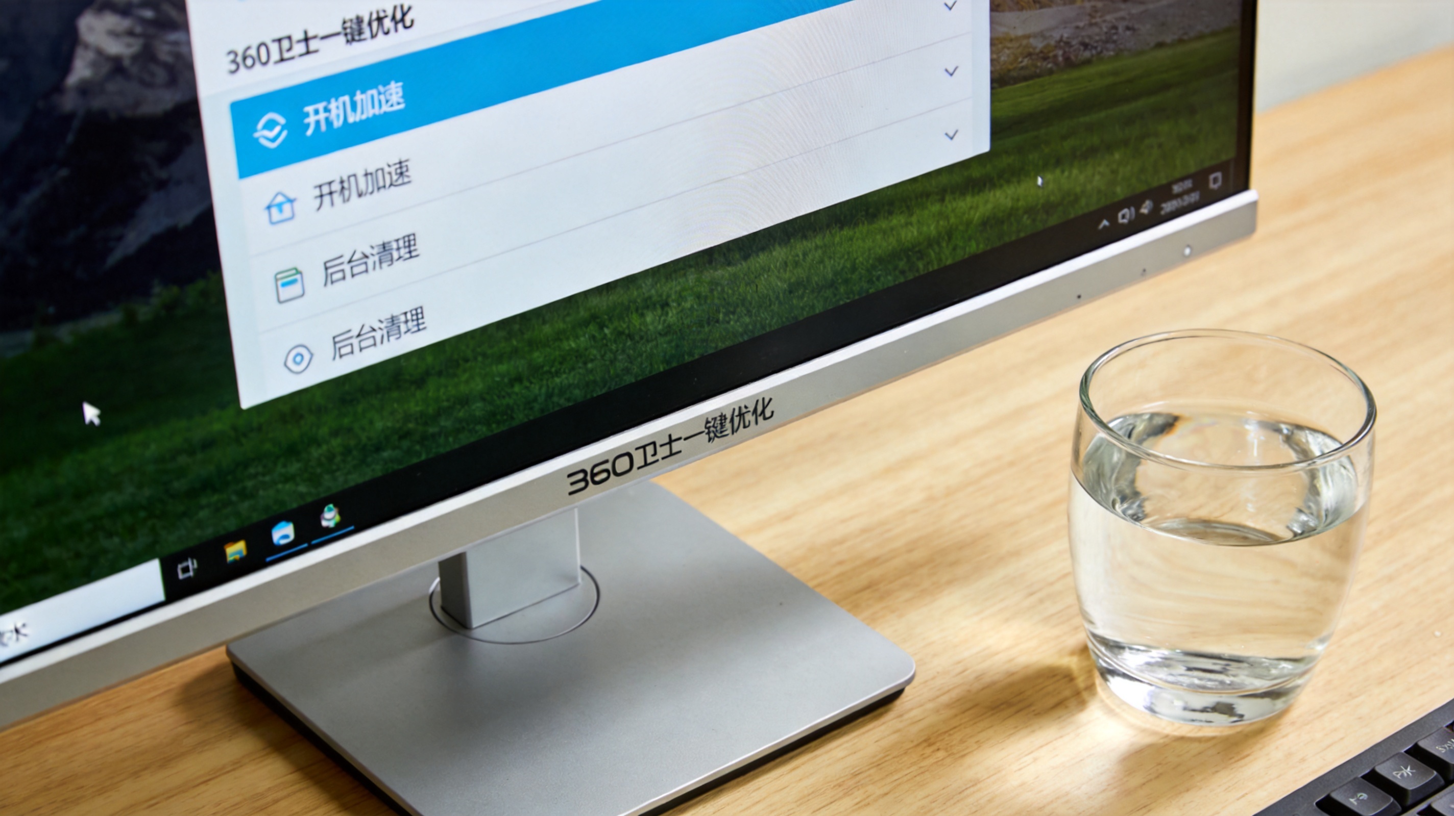 电脑桌面，屏幕显示360卫士一键优化界面，列表里分开机加速、后台清理板块，旁边放着半杯凉水，室内自然光