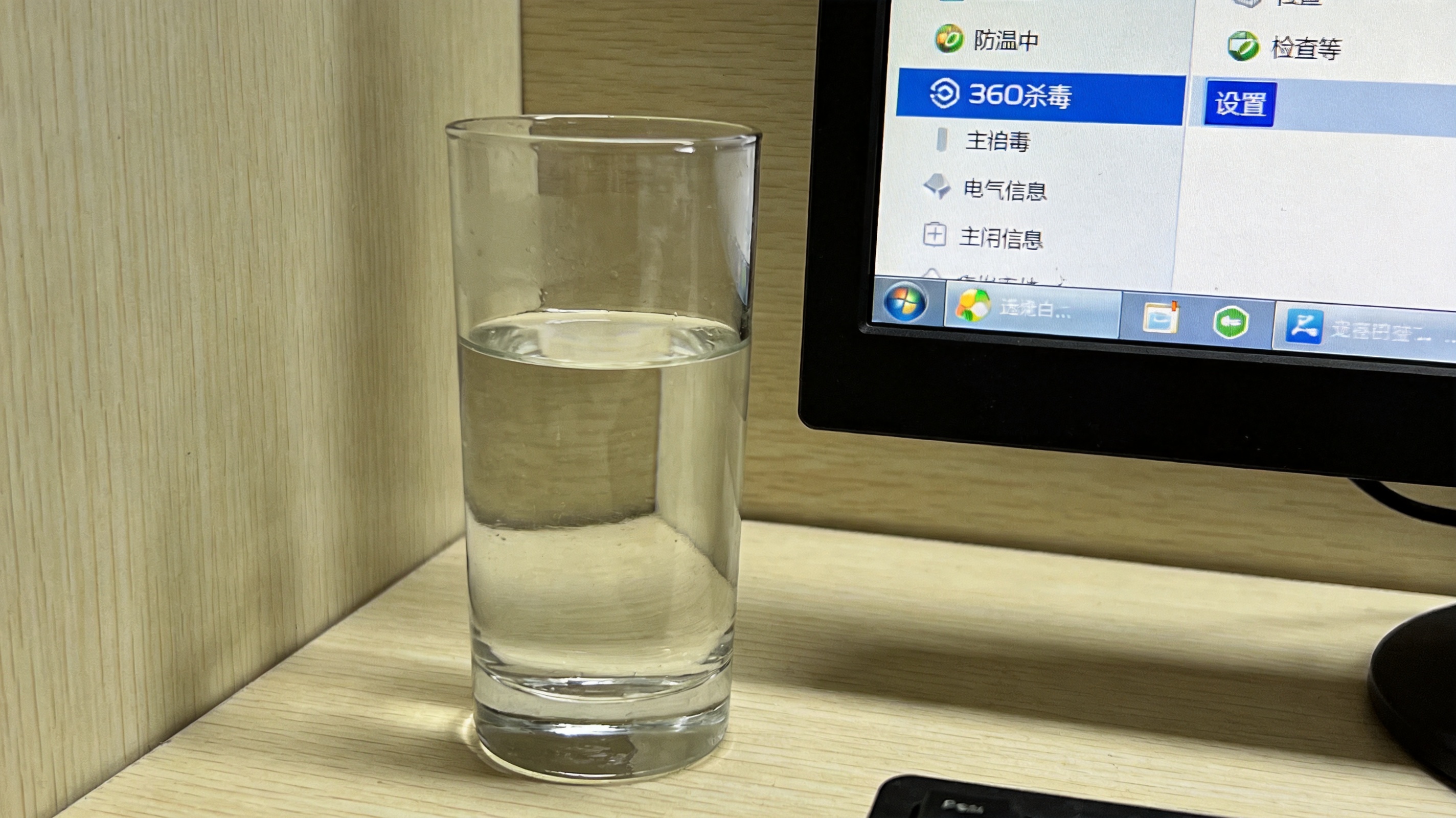 电脑桌面，屏幕显示360杀毒软件主界面，右上角设置按钮处于选中状态，旁边放着一杯常温的白水，室内自然光