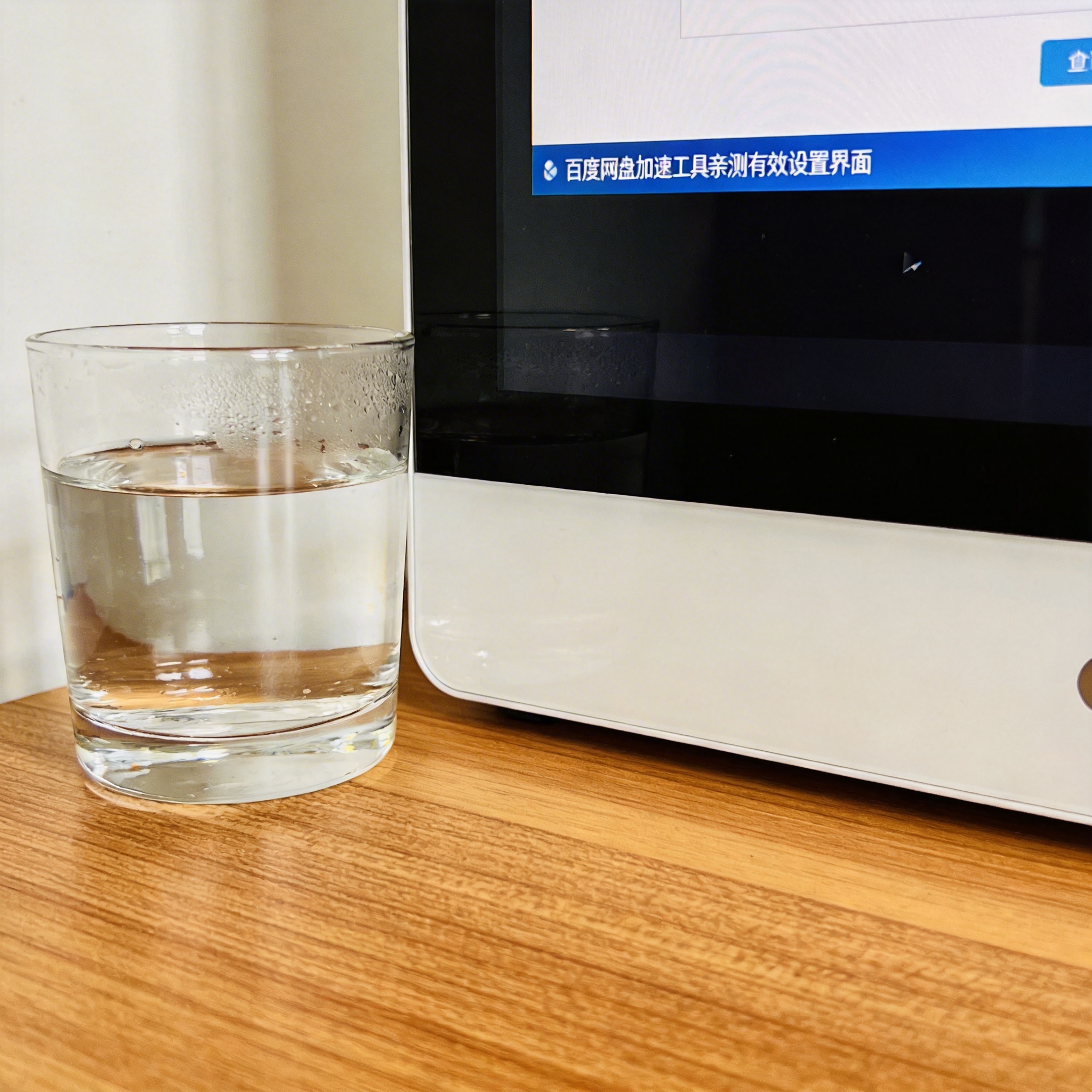 书桌上的主机，屏幕显示百度网盘加速工具亲测有效设置界面，桌角放着水杯，自然光