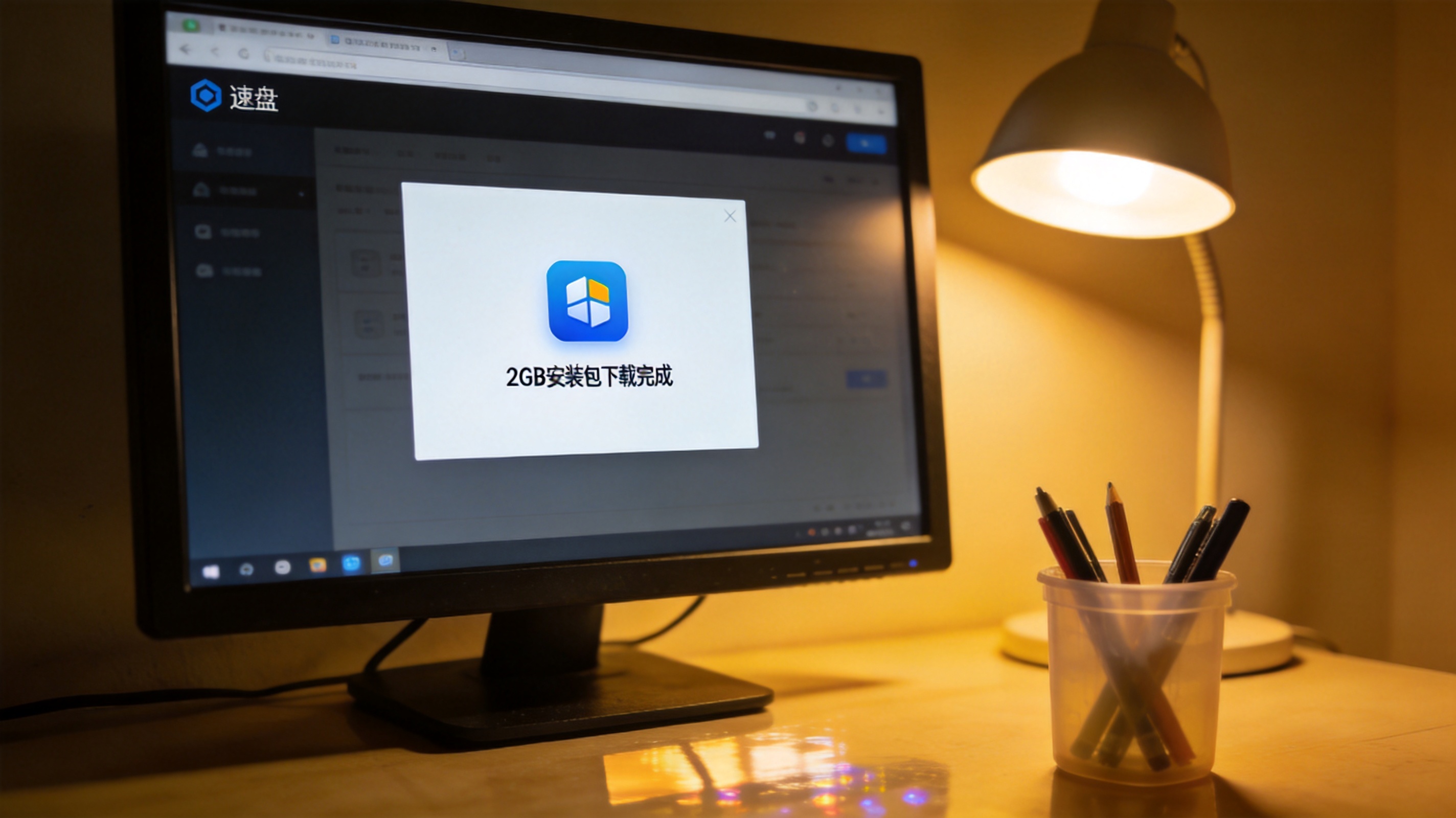 电脑屏幕显示速盘软件界面，界面上有2GB安装包的下载完成提示，桌面角落放着一个普通塑料笔筒，台灯暖光