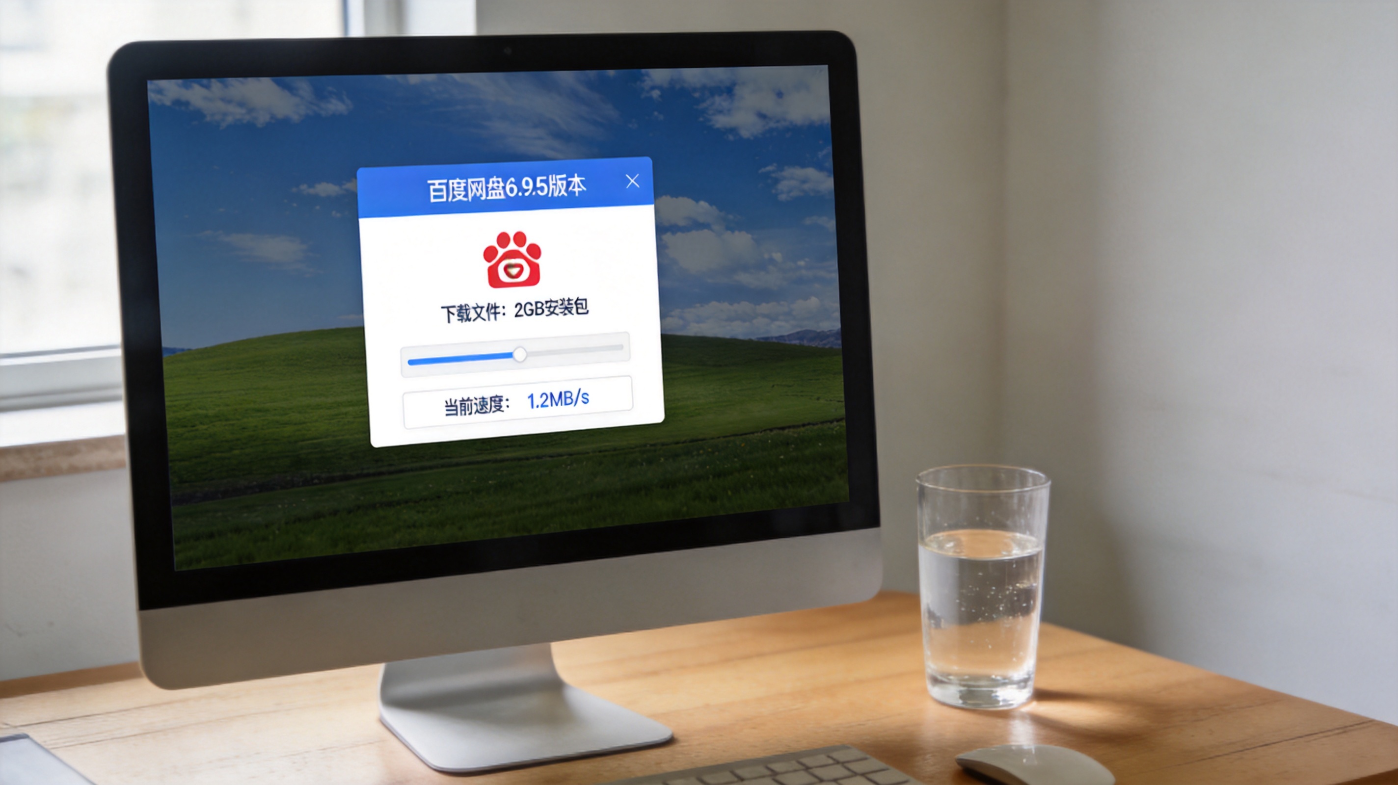 电脑桌面，屏幕显示百度网盘6.9.5版本的普通下载任务界面，下载文件为2GB安装包，当前速度显示1.2MB/s，旁边放着半杯凉白开，室内自然光